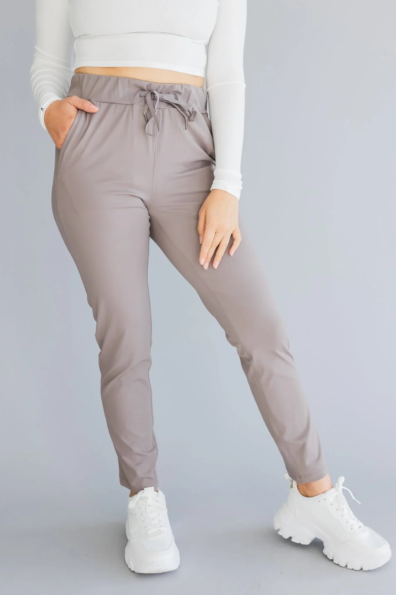 Woman wearing taupe joggers with drawstring waist, white crop top, and white sneakers