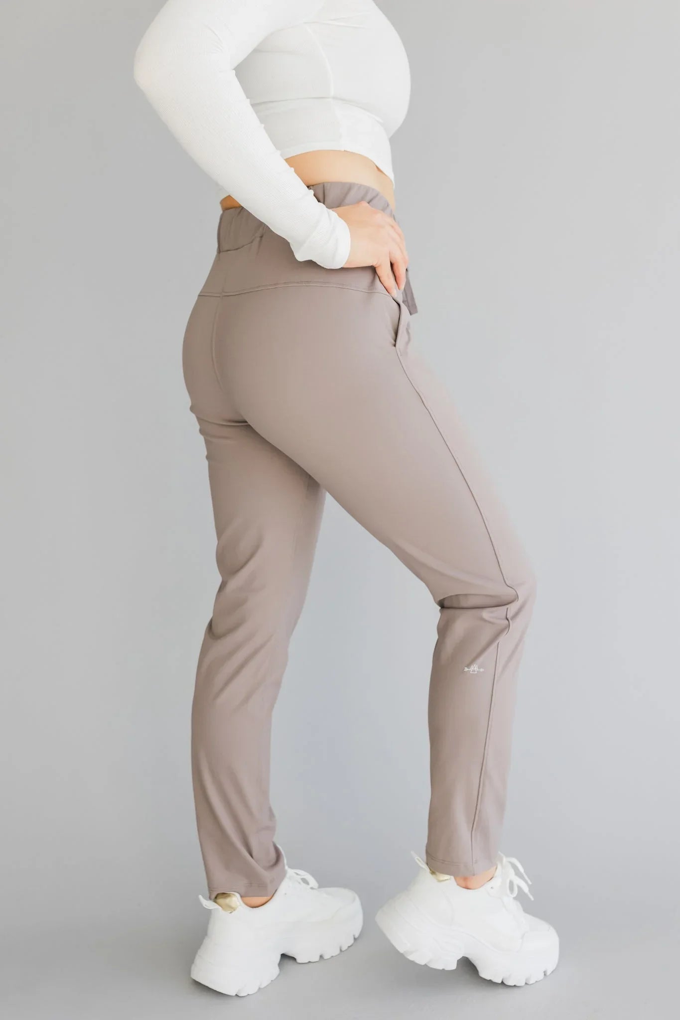 Woman wearing taupe jogger pants, white cropped long sleeve top, and chunky white sneakers