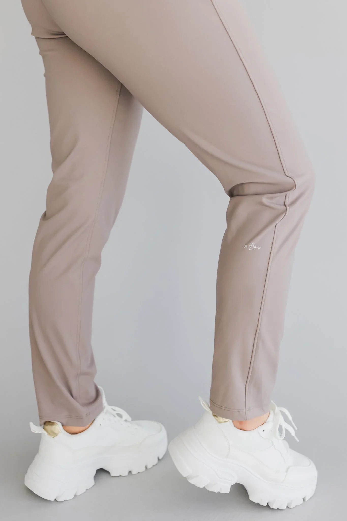 Taupe athletic pants with white chunky sneakers on grey background