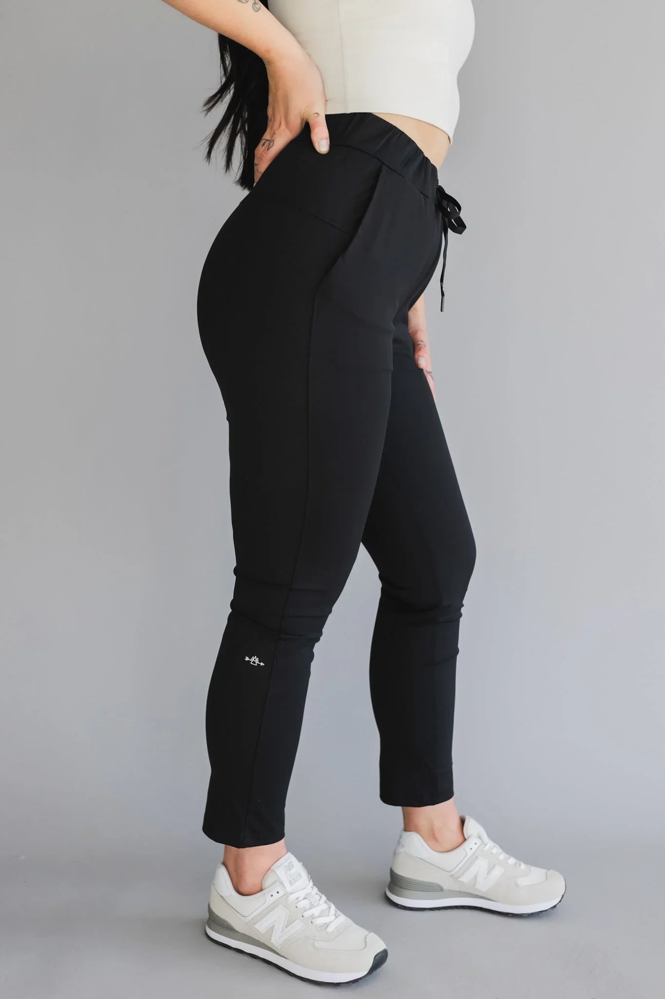 Woman wearing black jogger pants and white sneakers on a gray background