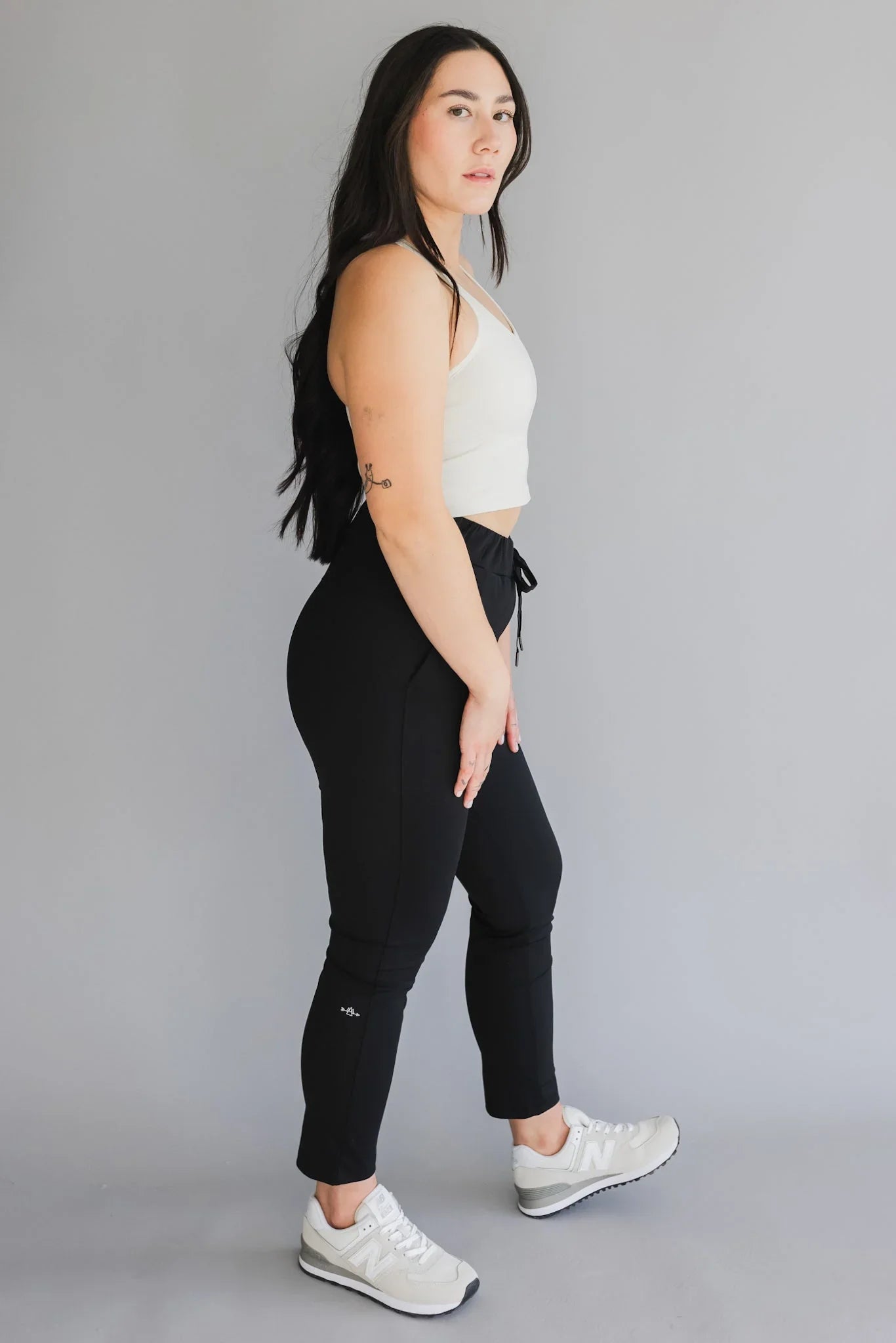 Woman in white crop top and black jogger pants posing in studio, casual activewear fashion
