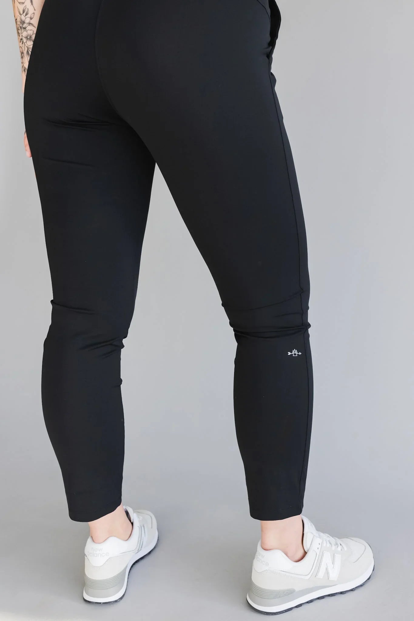 Back view of person wearing black leggings and white New Balance sneakers on a grey backdrop