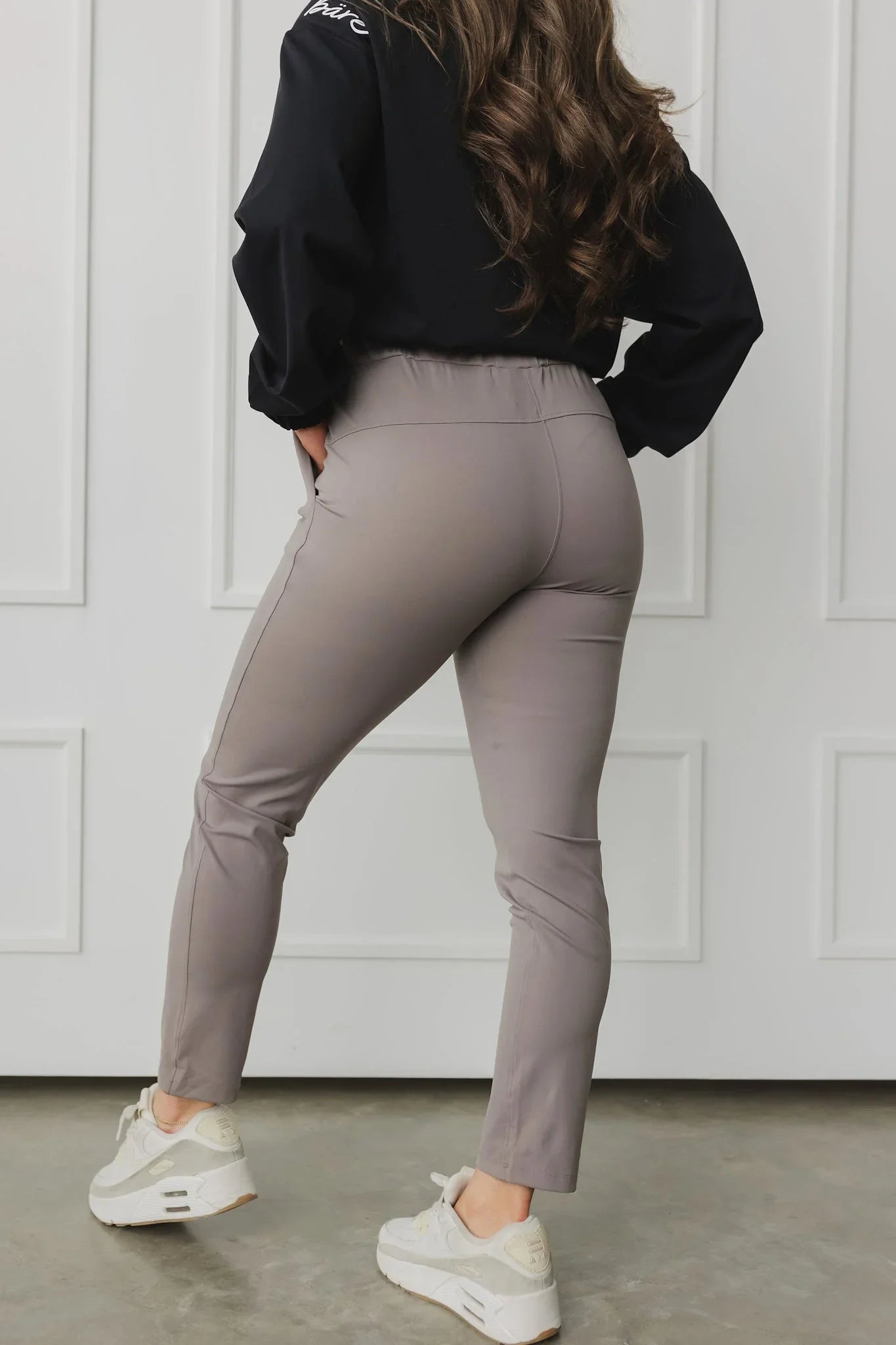 Woman wearing taupe high-waisted pants, white sneakers, and black top indoors