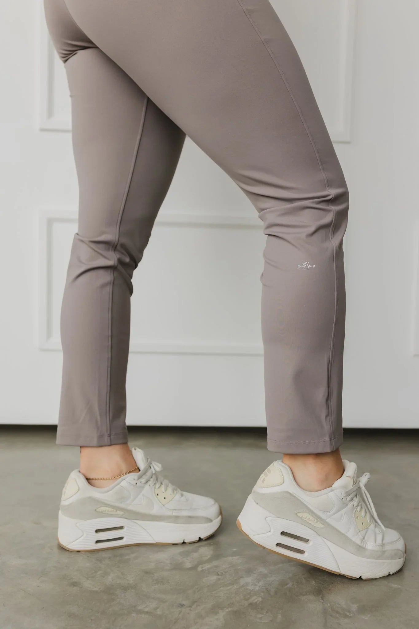 Taupe leggings with white sneakers on concrete floor, minimalist indoor setting