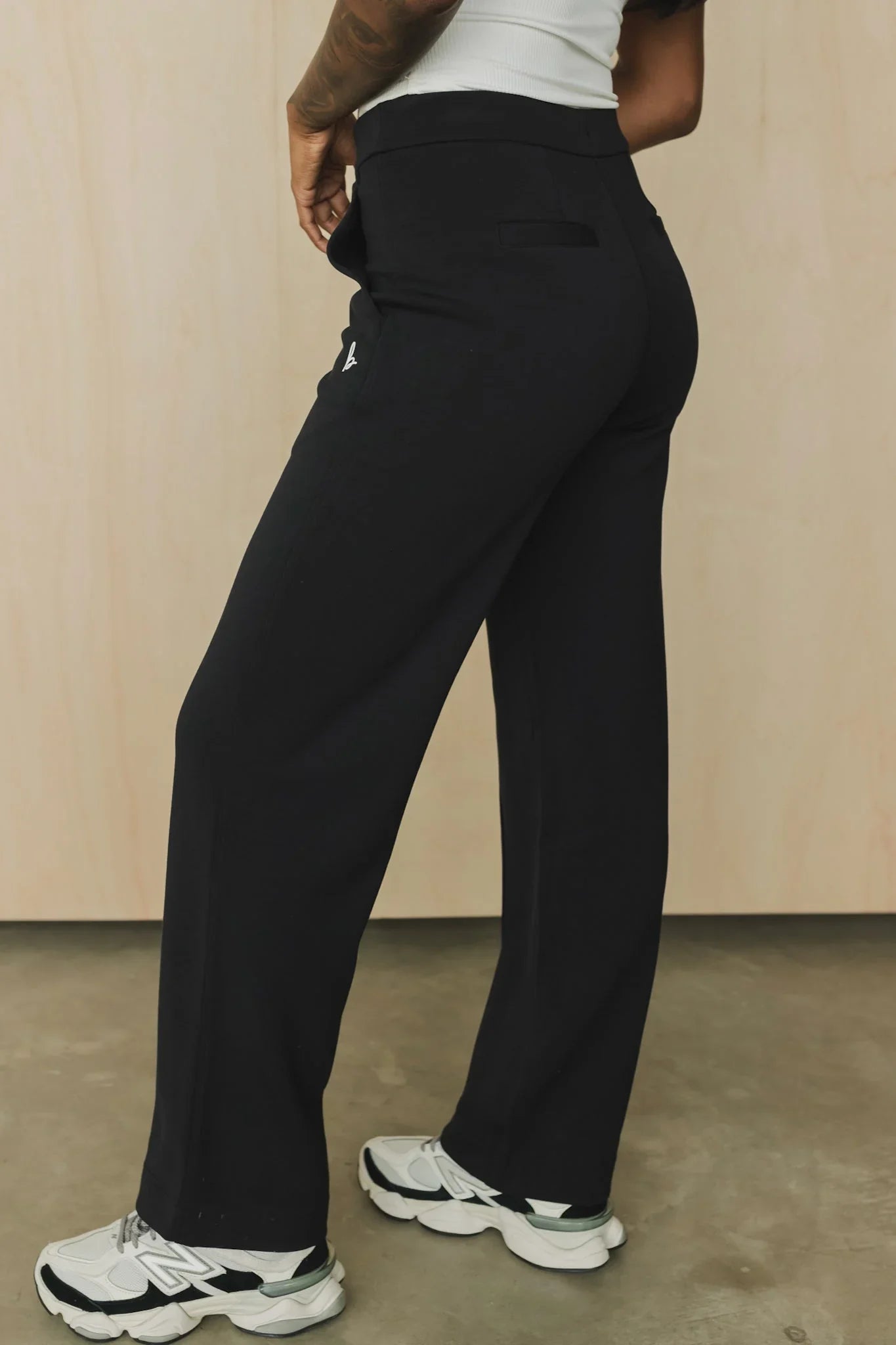 Woman wearing black wide-leg pants, white tank top, and white sneakers indoors