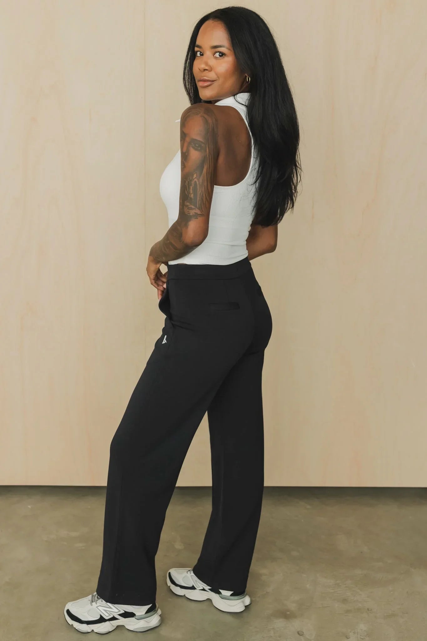 Woman in white sleeveless top, black wide-leg pants, and white sneakers posing indoors