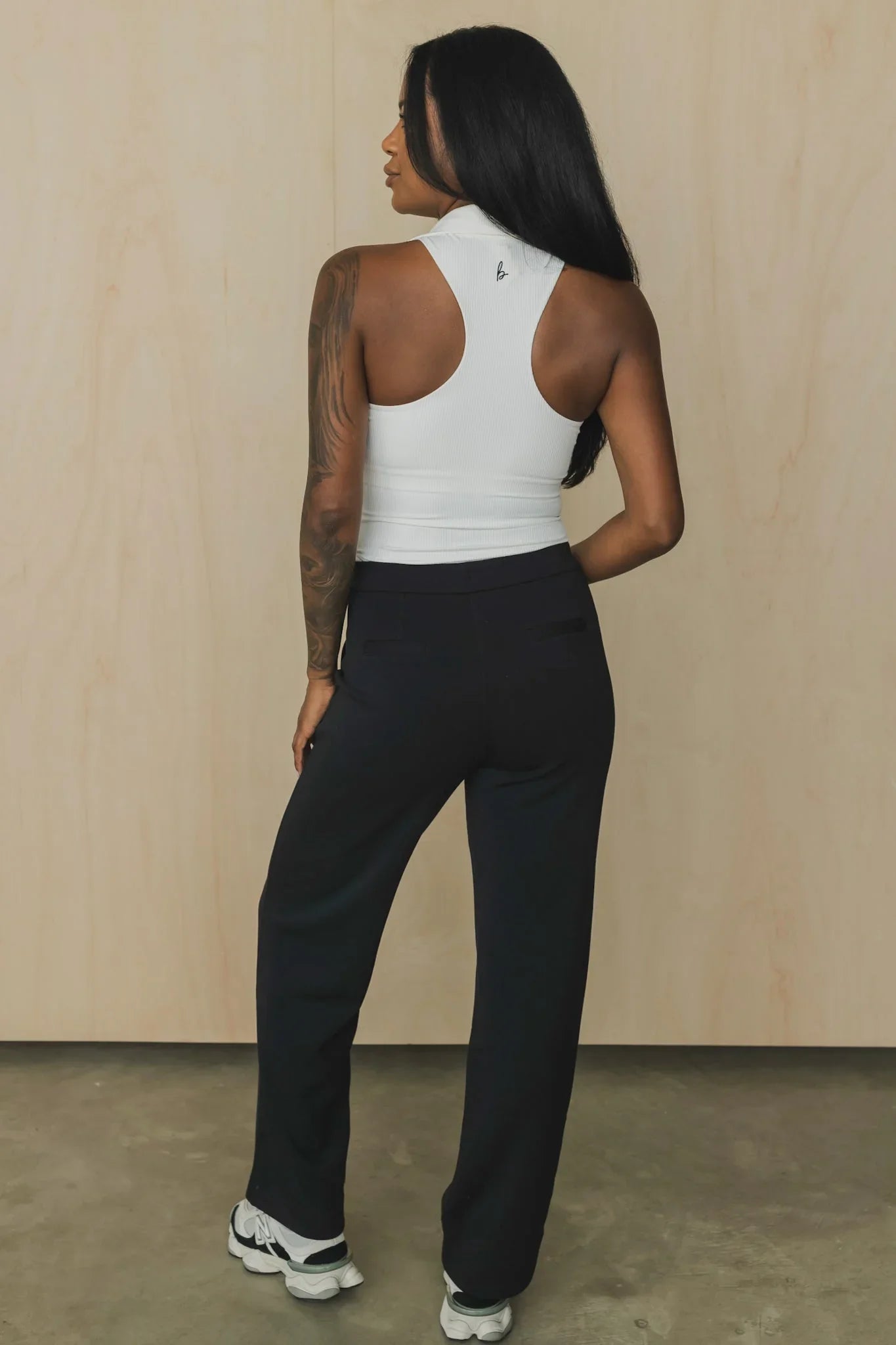 Woman in white ribbed racerback tank top, black pants, and sneakers, standing indoors
