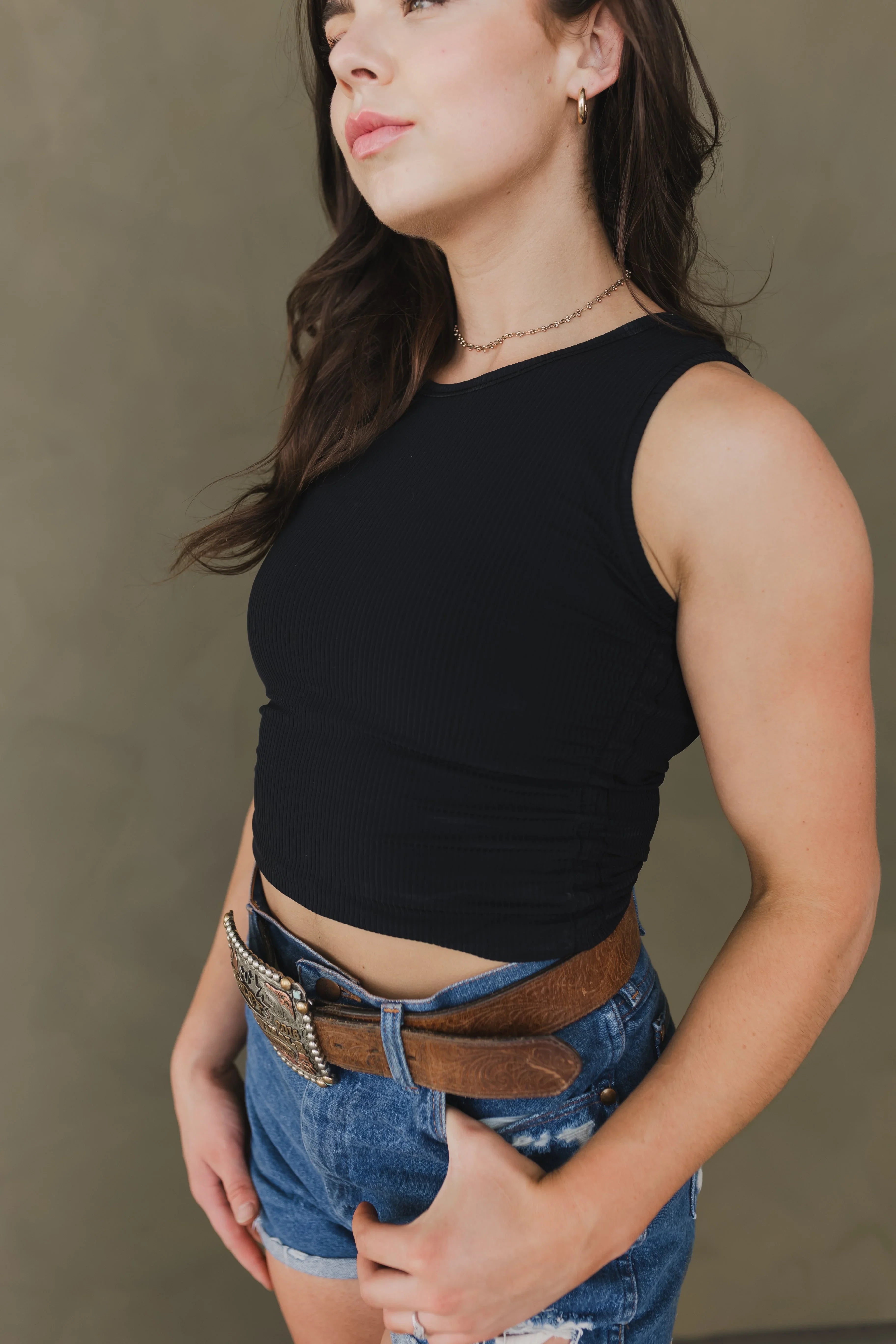 Woman in black sleeveless top and denim shorts with brown tooled leather belt