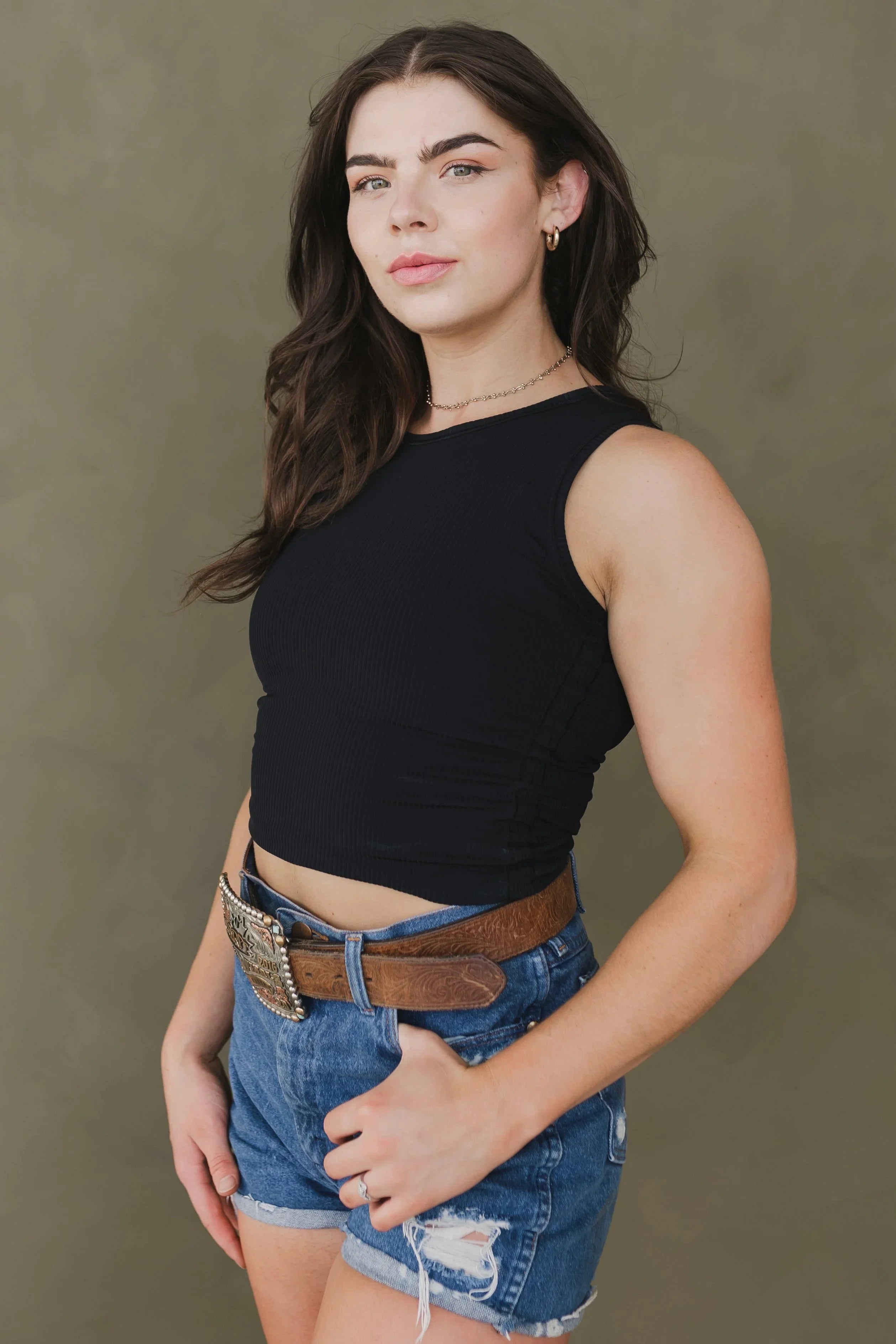 Woman in black sleeveless top, denim shorts, brown tooled western belt, gold jewelry