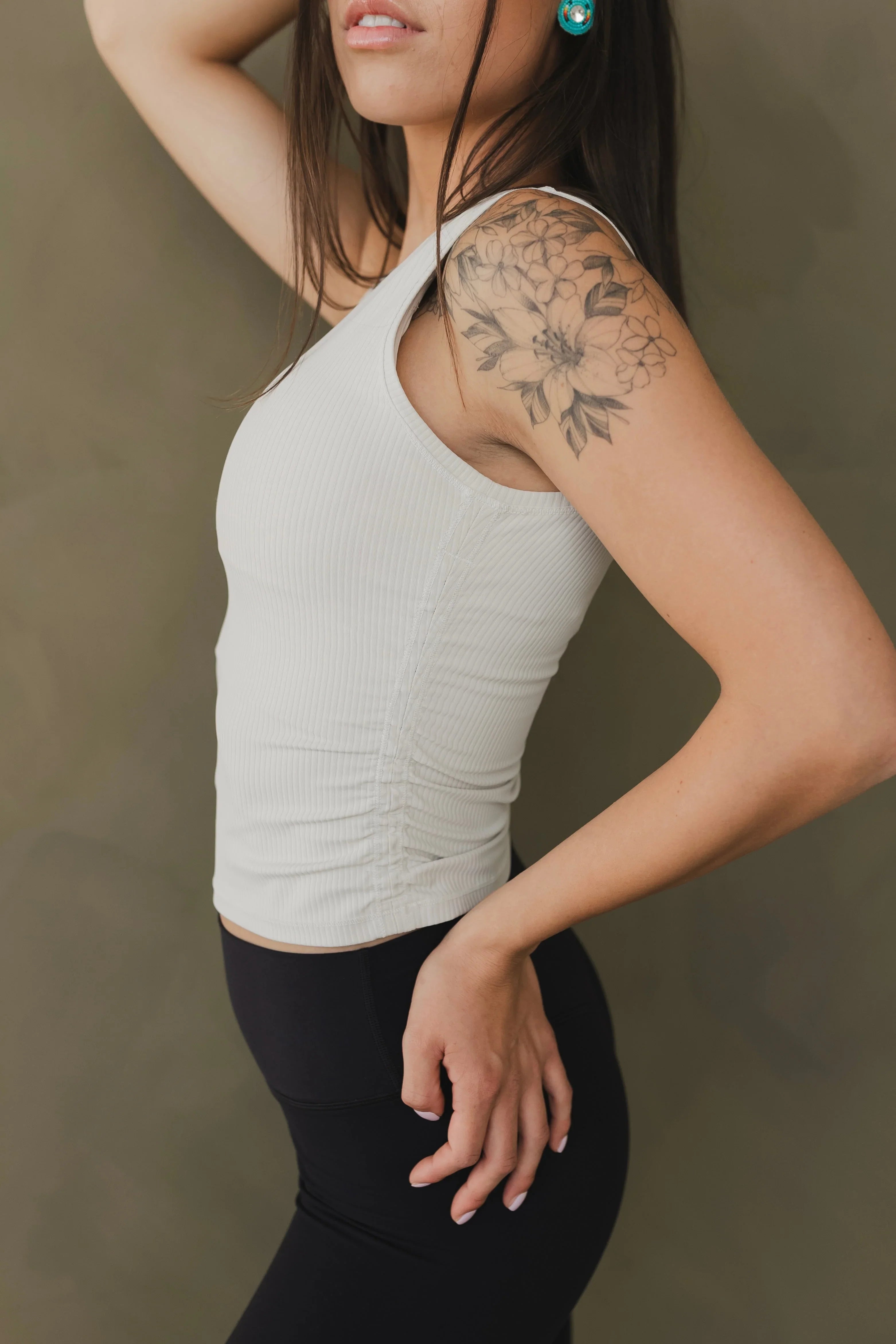 Woman in white ribbed tank top with floral shoulder tattoo and black leggings
