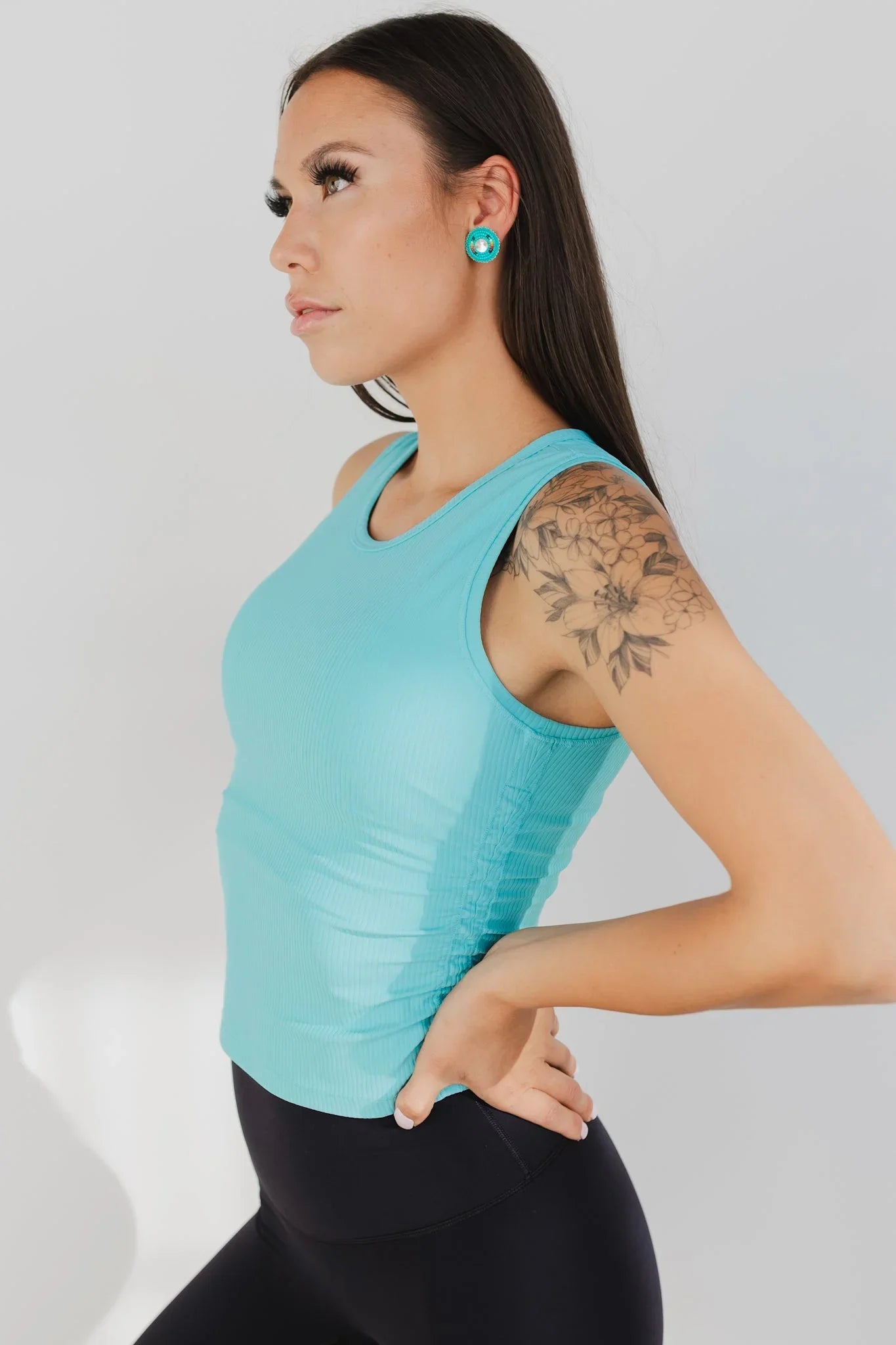 Woman in turquoise tank top, floral arm tattoo, black leggings, turquoise earrings