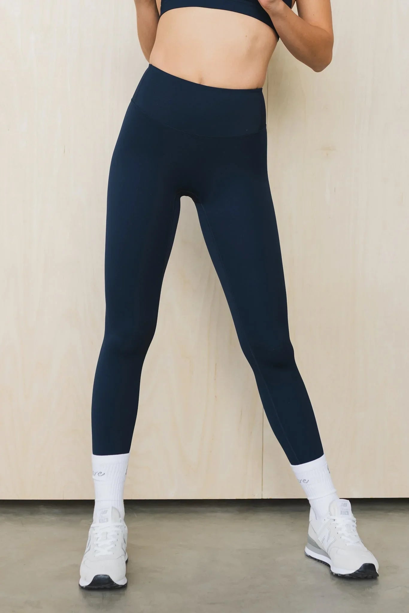 Woman wearing high-waisted navy blue leggings, white socks, and white sneakers indoors