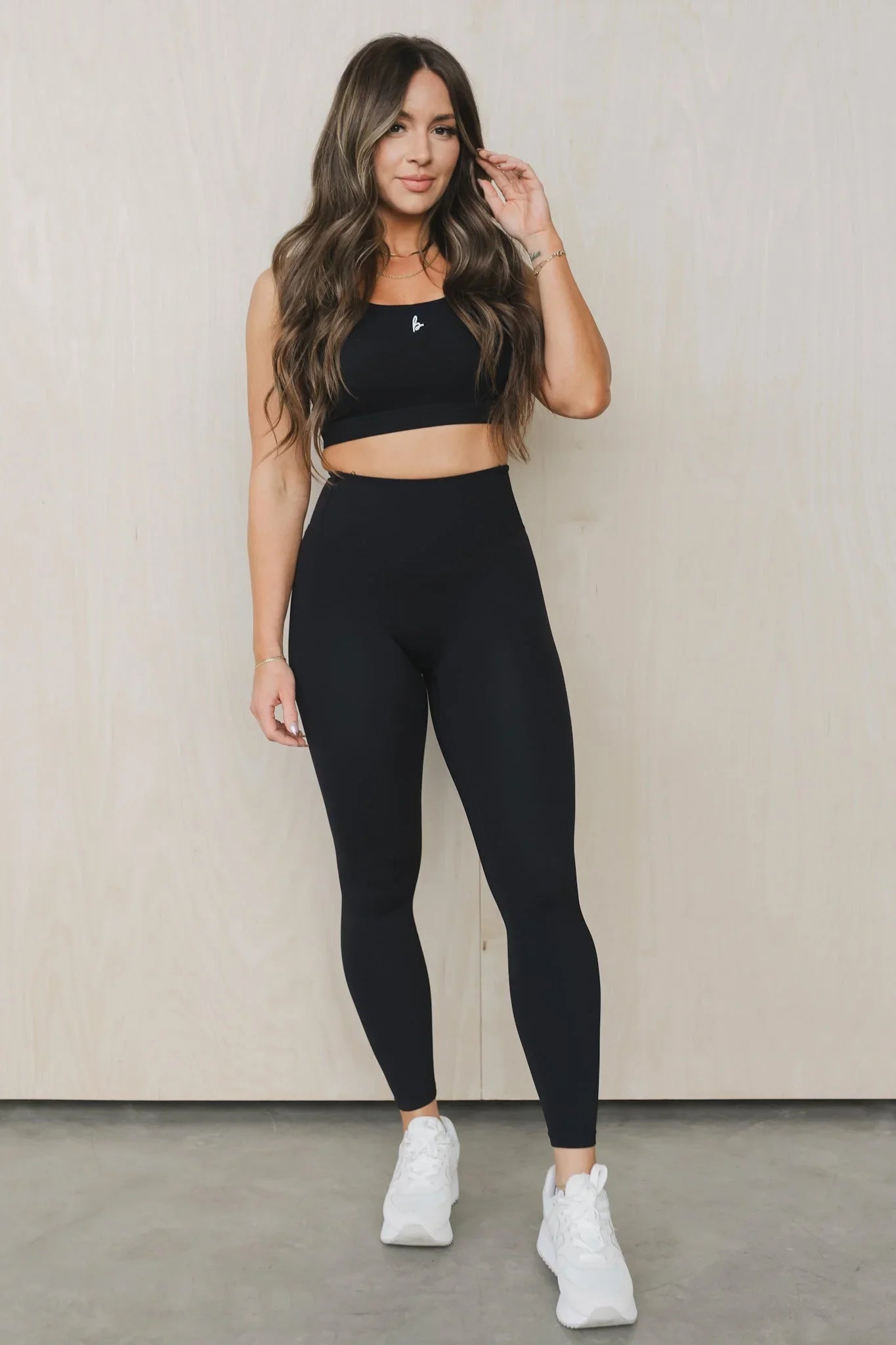Woman in black workout leggings and crop top, white sneakers, standing indoors