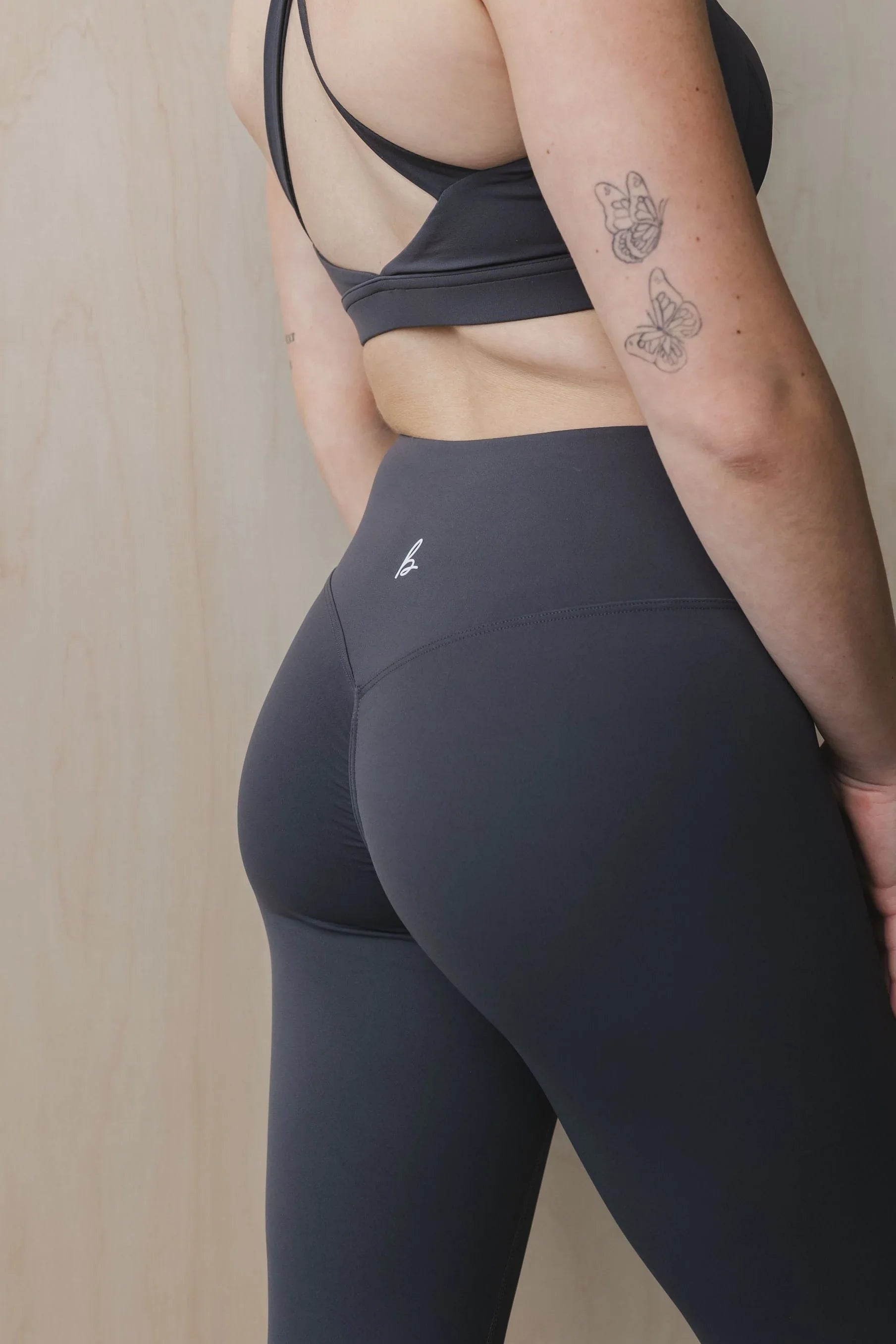 Woman in black high-waisted leggings and sports bra, butterfly tattoos on arm