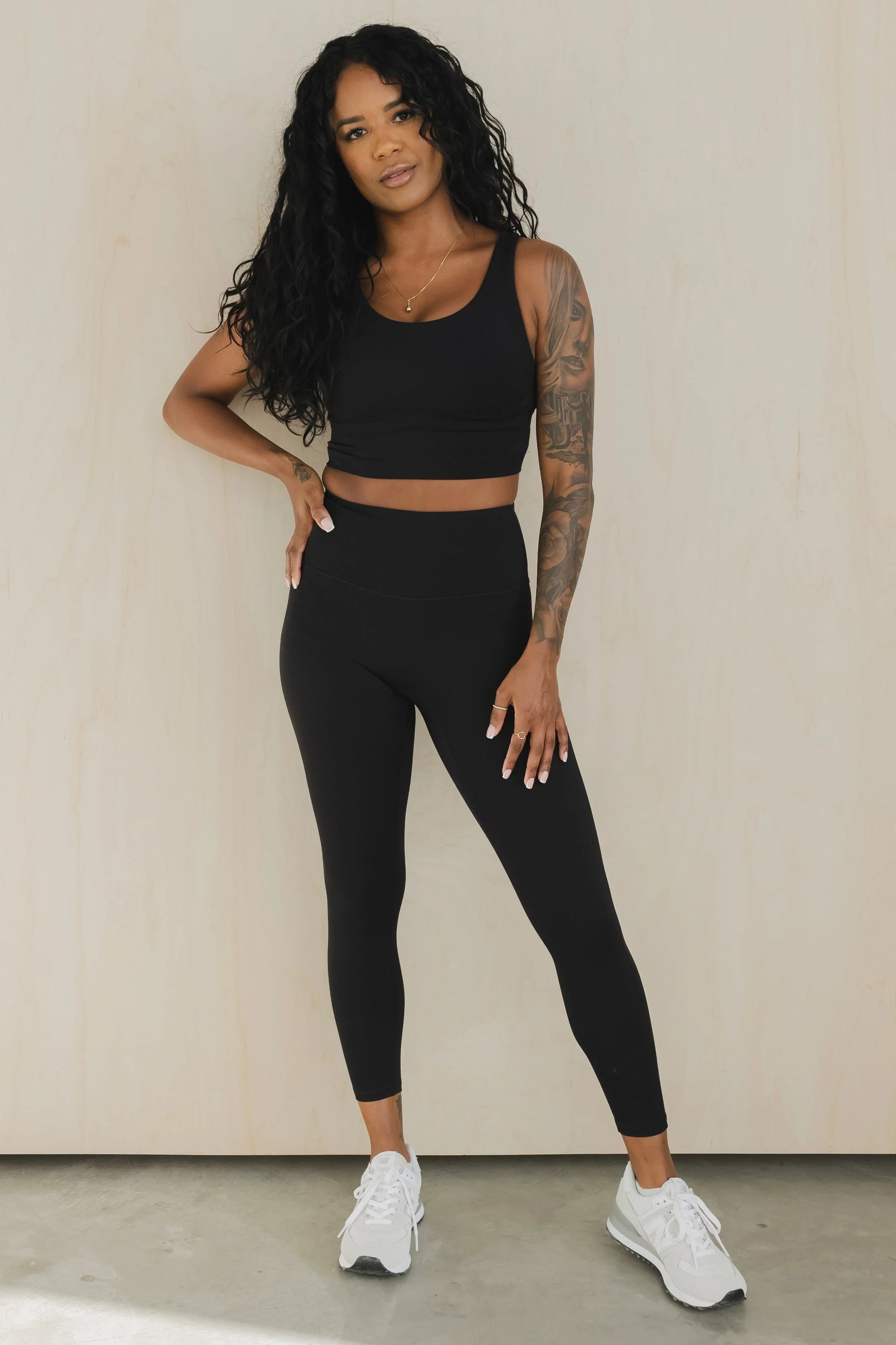 Woman in black sports bra and high-waisted leggings, white sneakers, studio background
