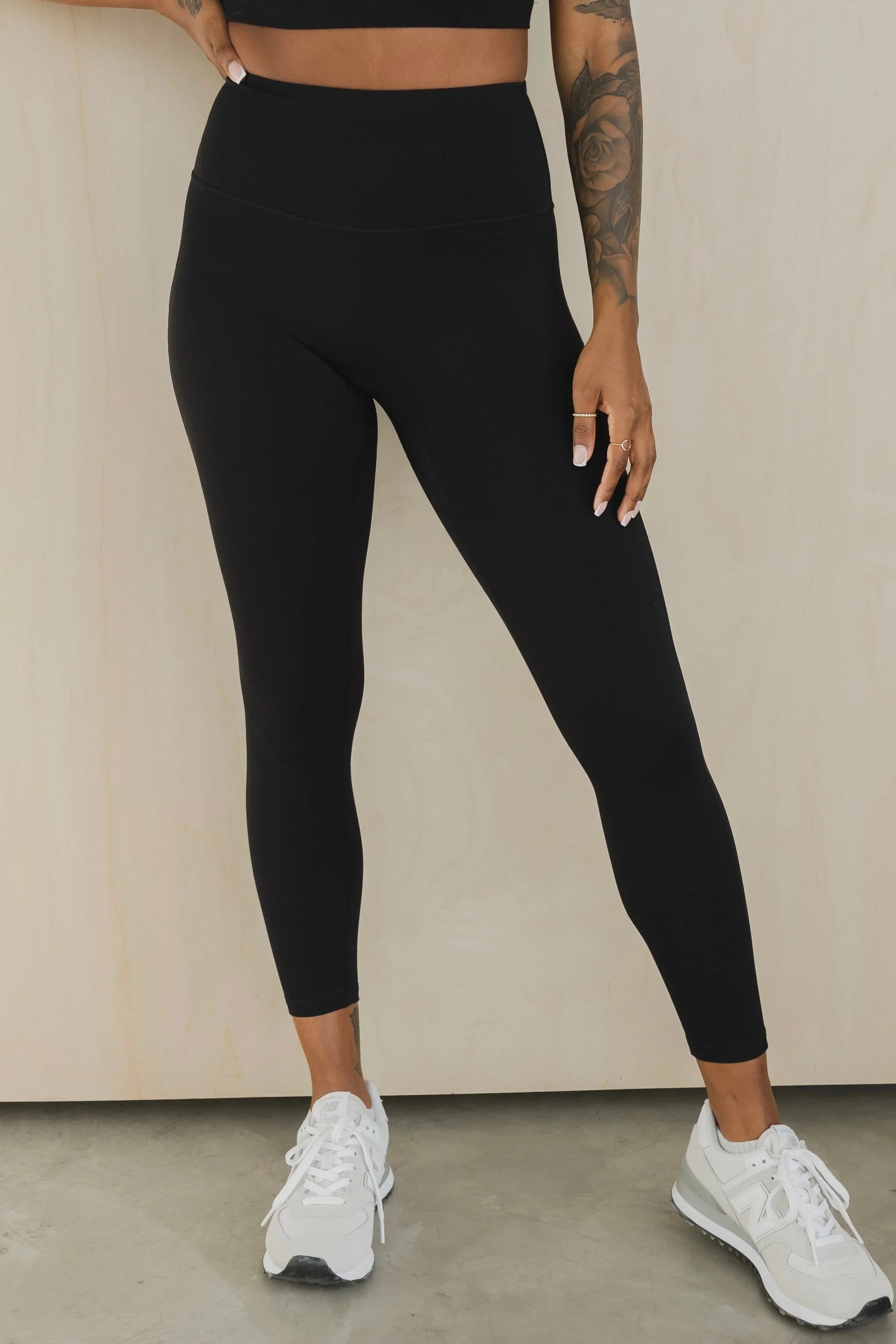 Woman wearing high-waisted black leggings and white sneakers, tattooed arm visible
