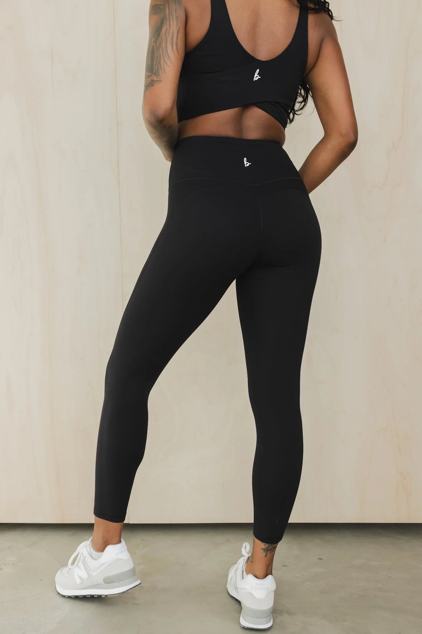 Woman in black high-waisted leggings and sports bra with white New Balance sneakers