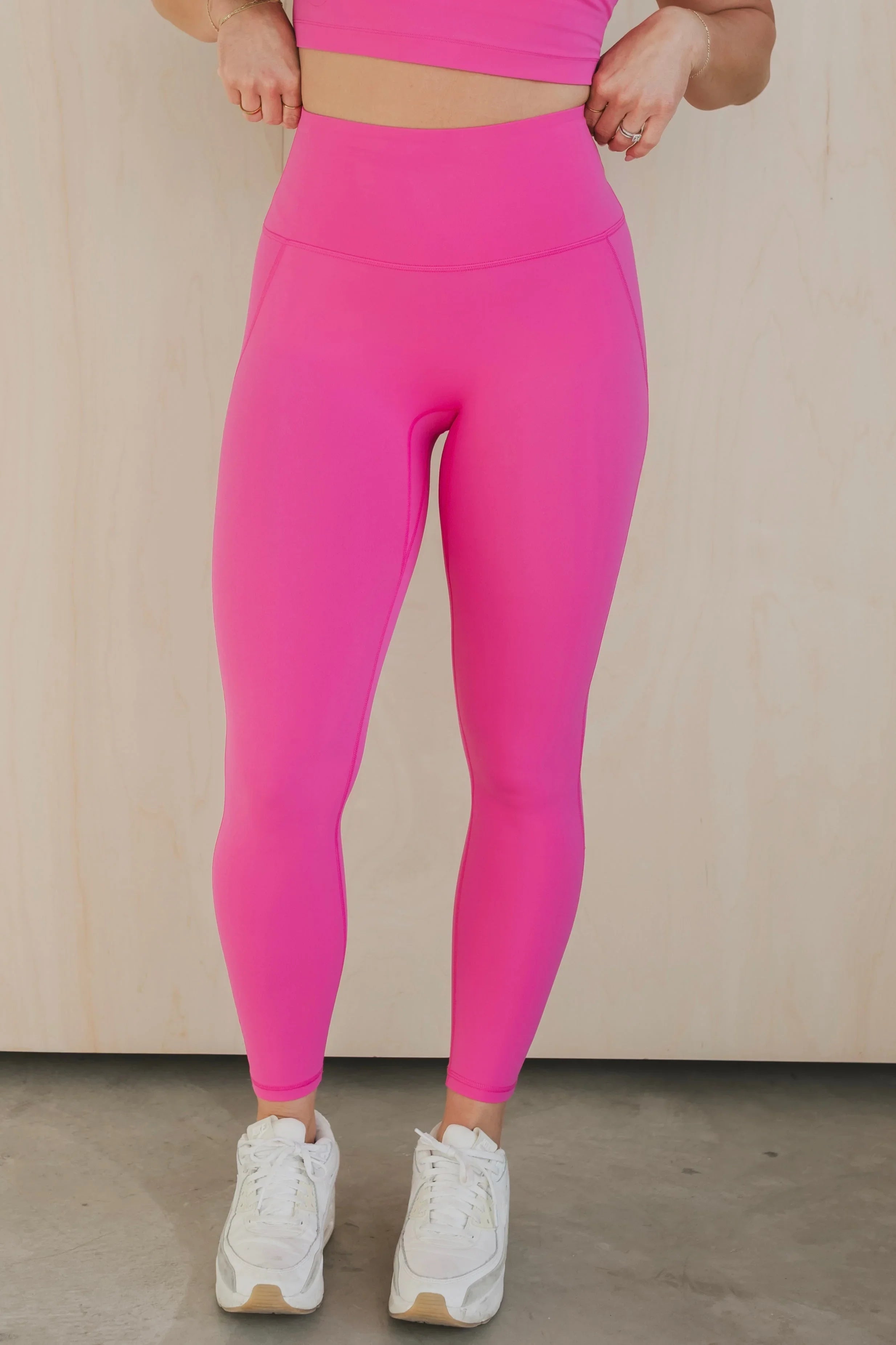 Woman wearing bright pink high-waisted leggings and white sneakers on concrete floor