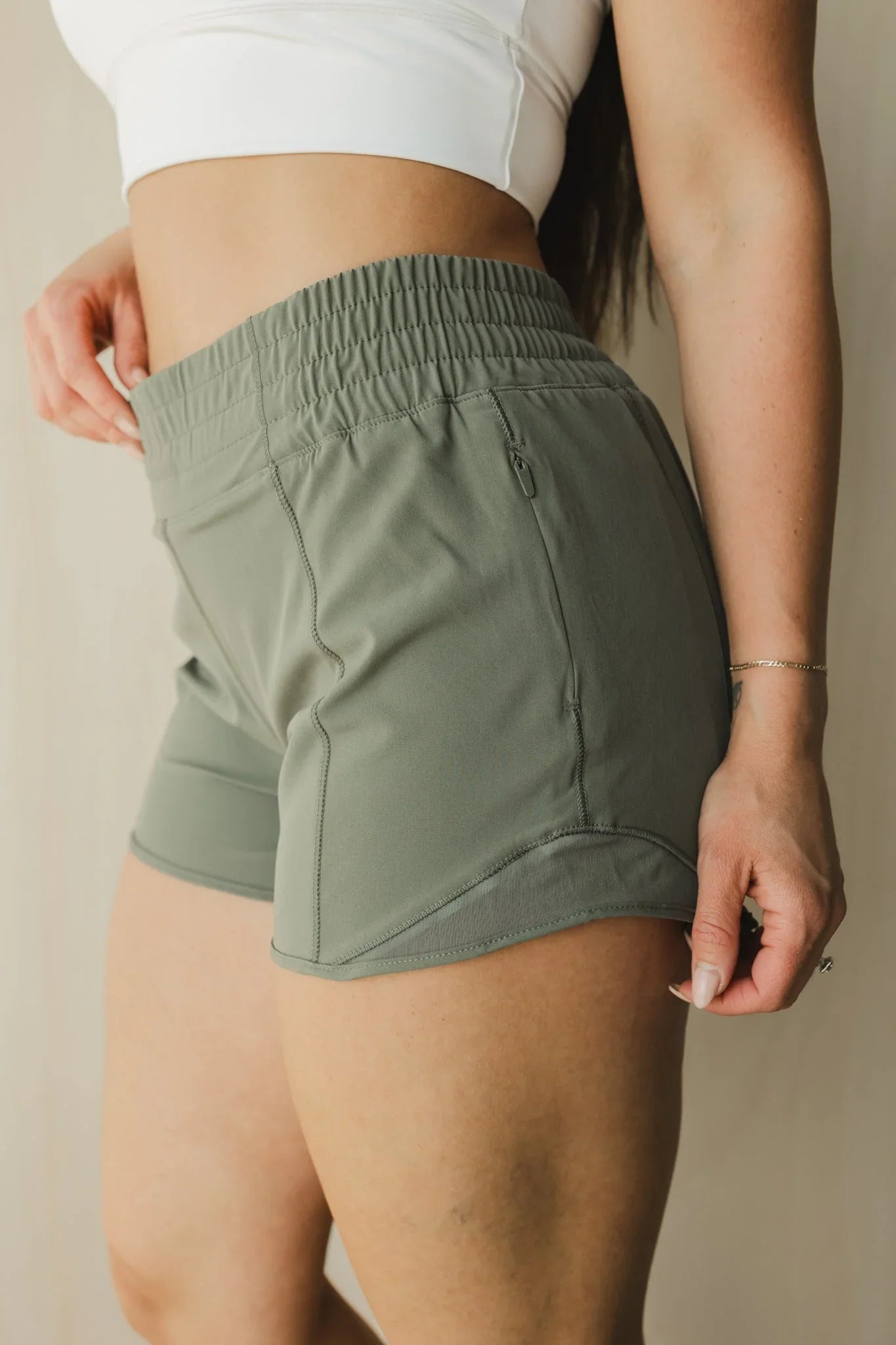Woman wearing olive green athletic shorts with side pocket and white crop top