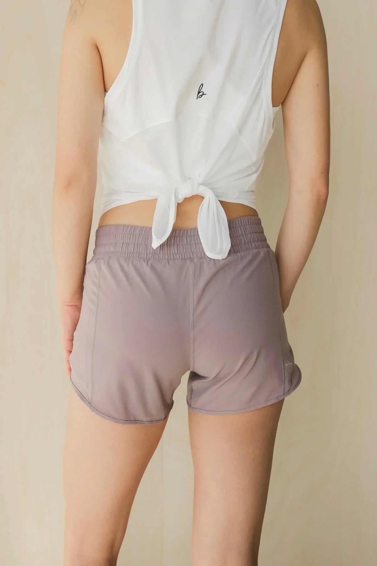 Woman wearing mauve athletic shorts and a white knotted tank top, back view