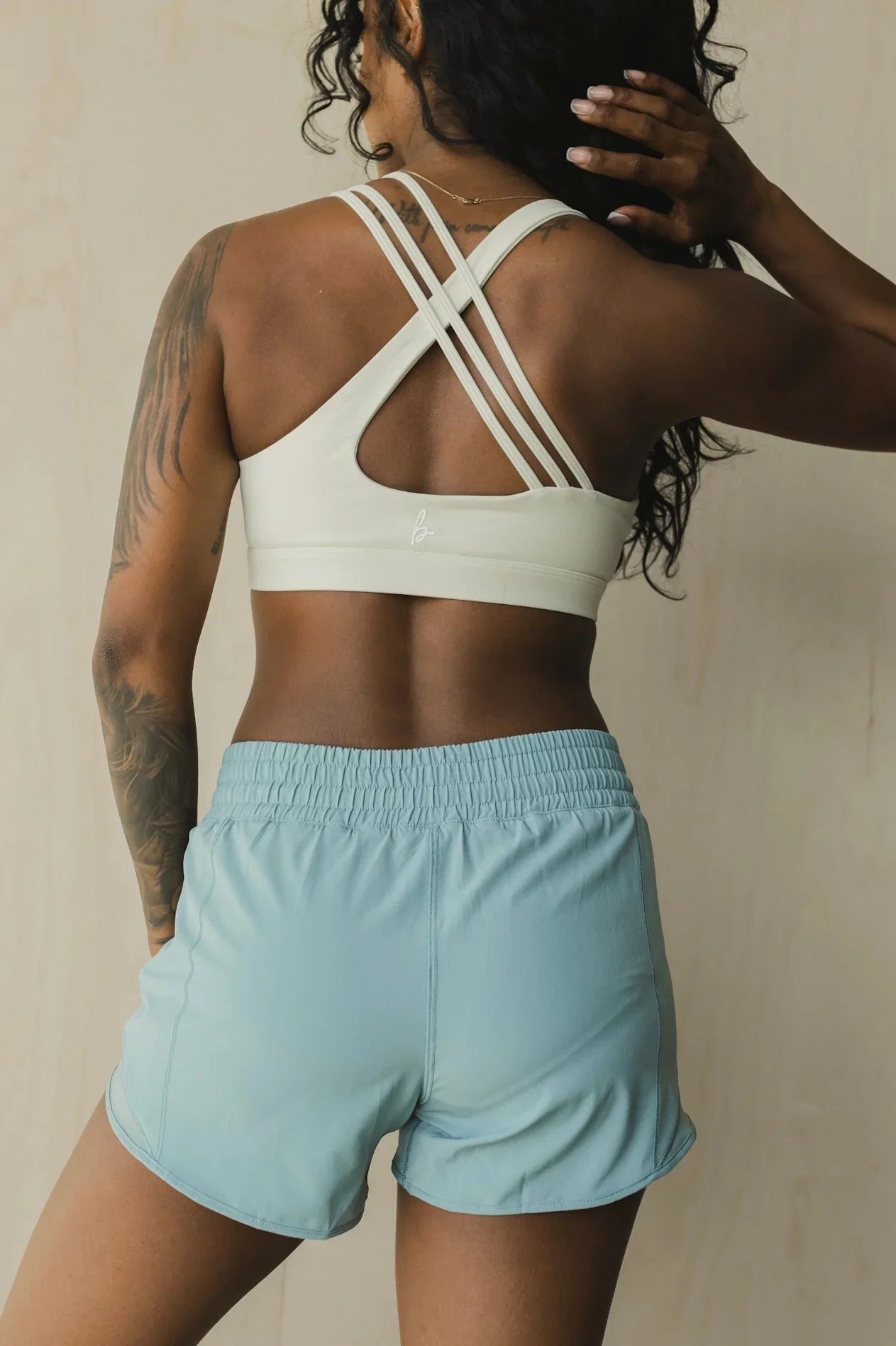 Woman in light blue athletic shorts and white strappy sports bra, back view