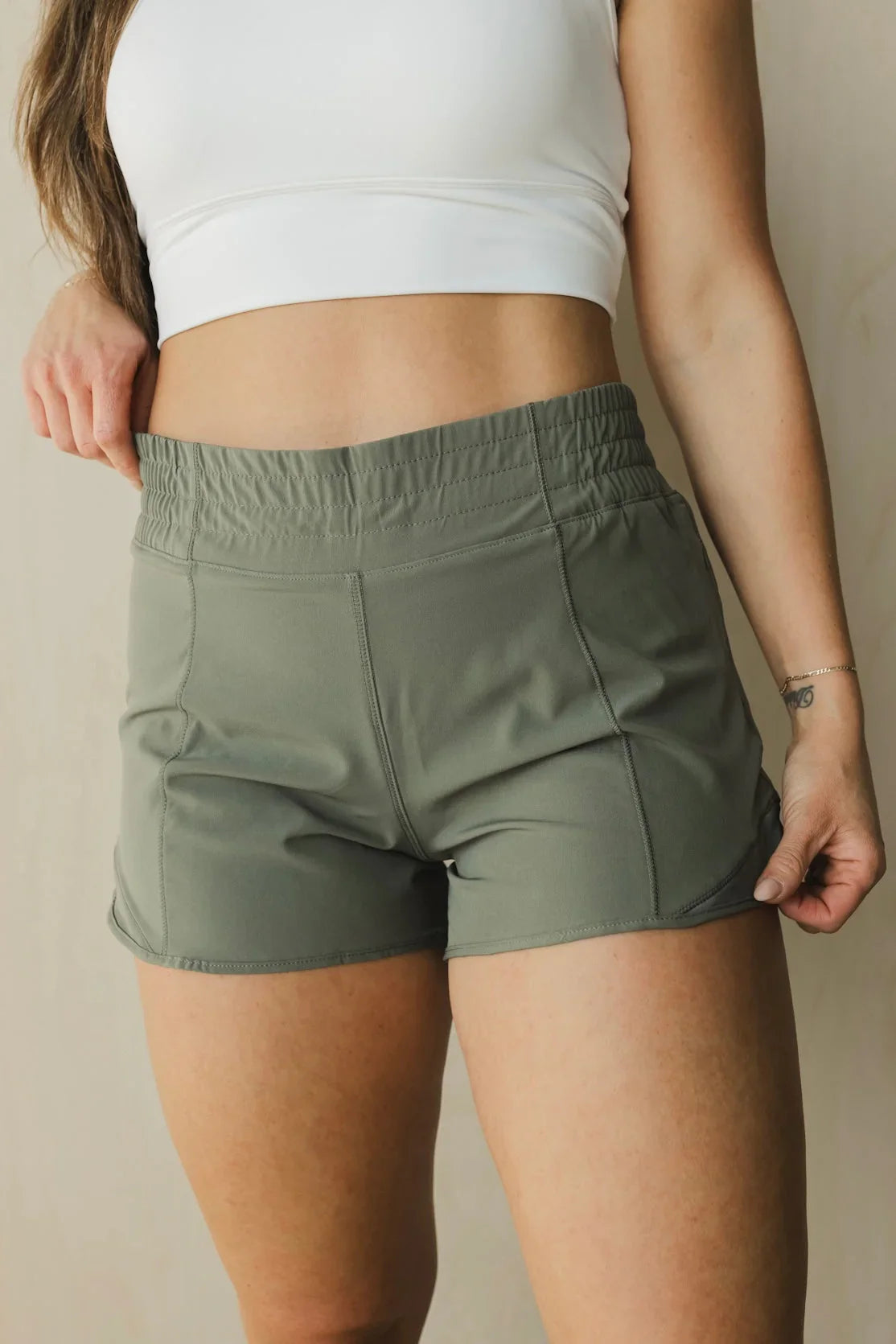 Woman wearing olive green athletic shorts and white crop top against neutral background