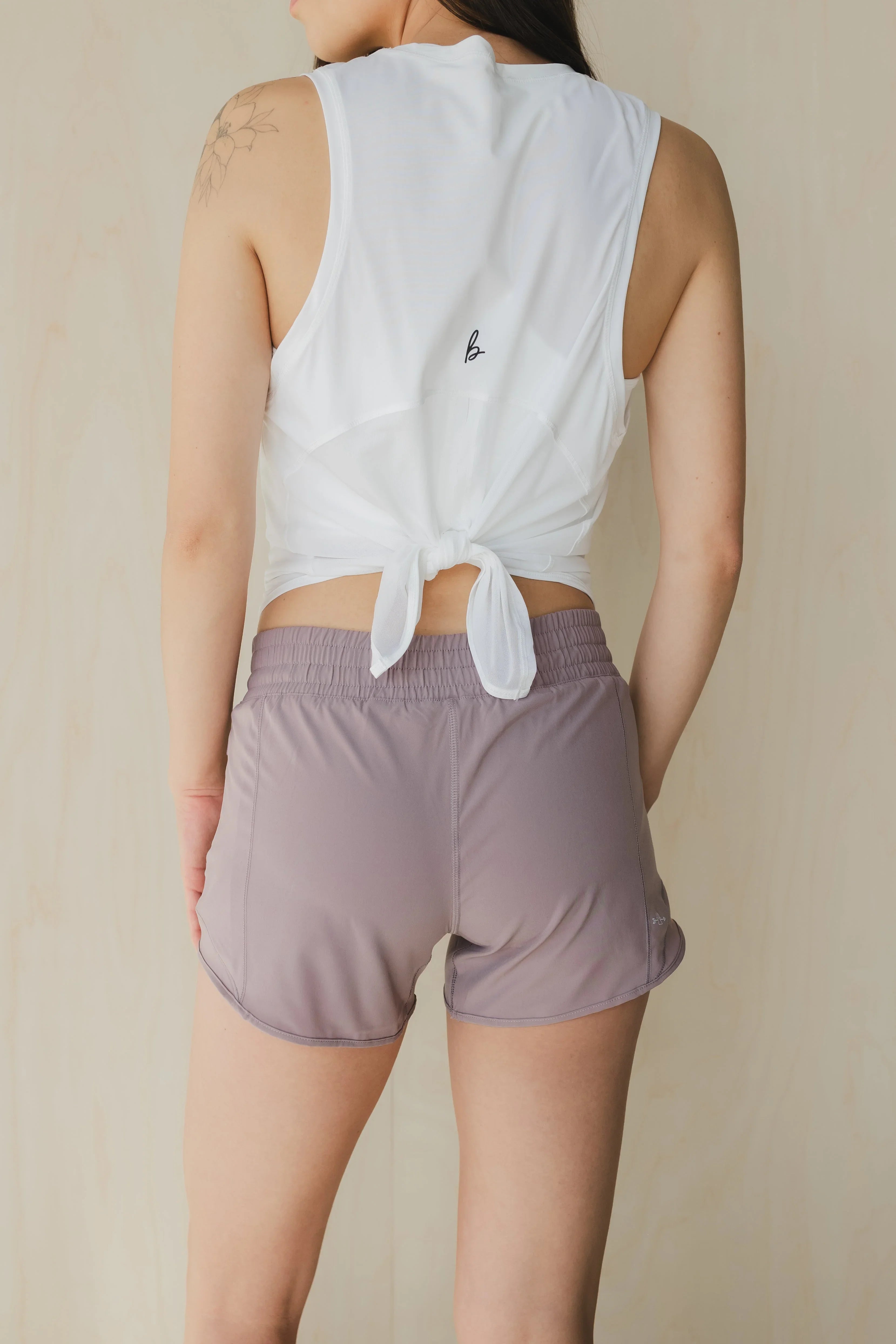 Woman in white tie-back tank top and mauve athletic shorts, showing floral arm tattoo