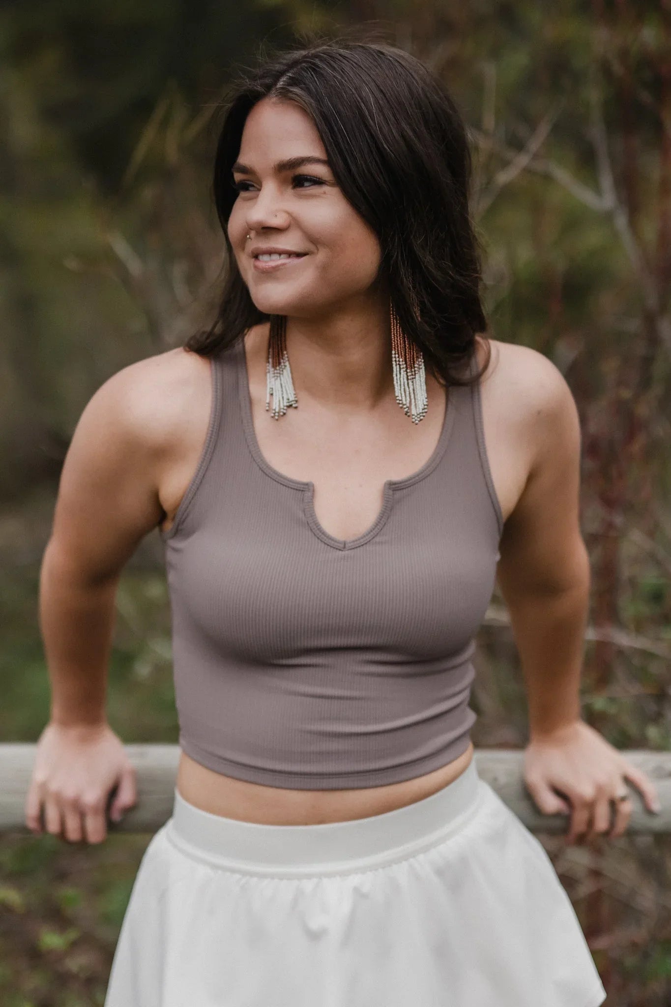 Woman outdoors wearing taupe crop top, white skirt, and long beaded earrings