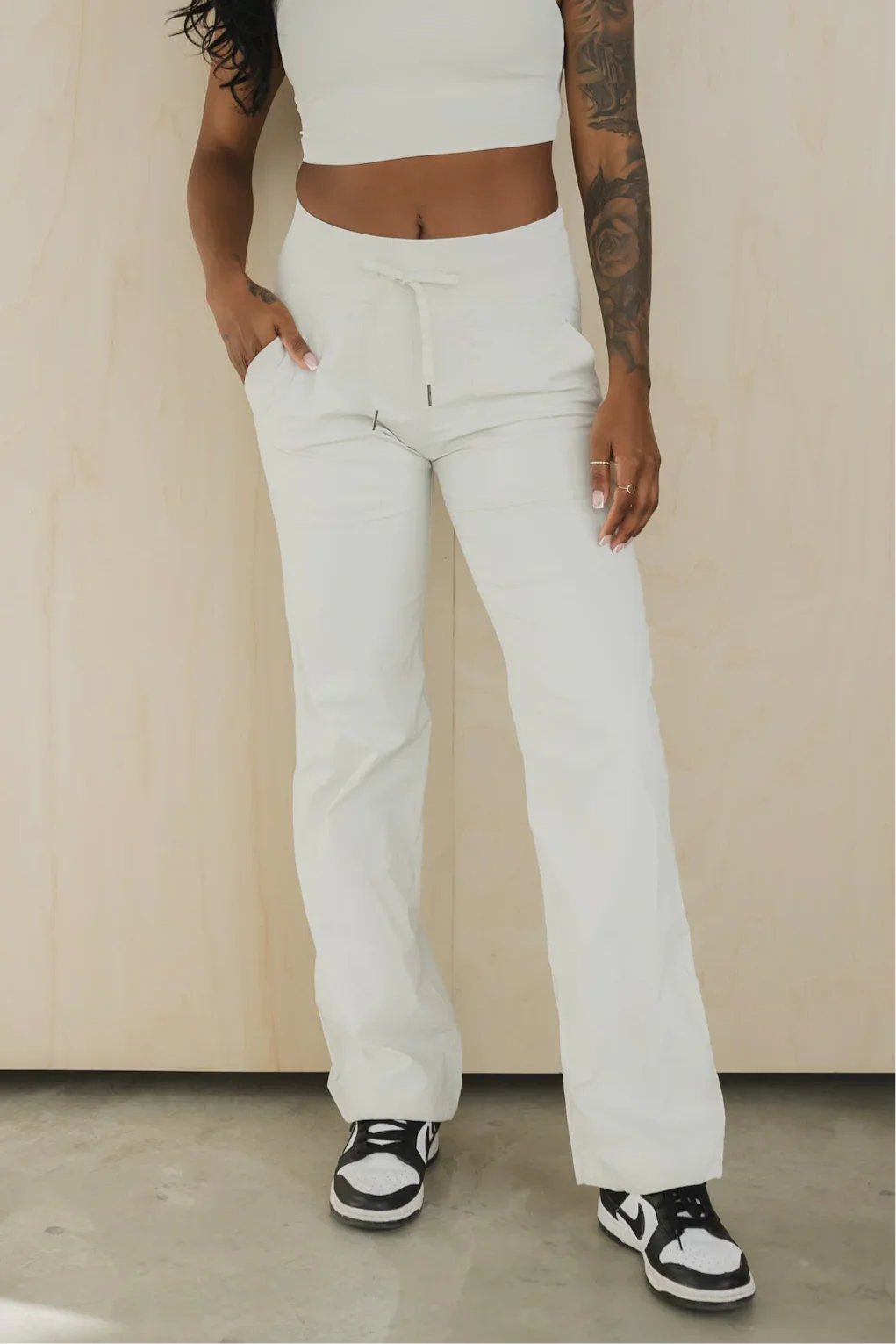Woman in white drawstring pants and crop top with black and white sneakers, tattooed arm