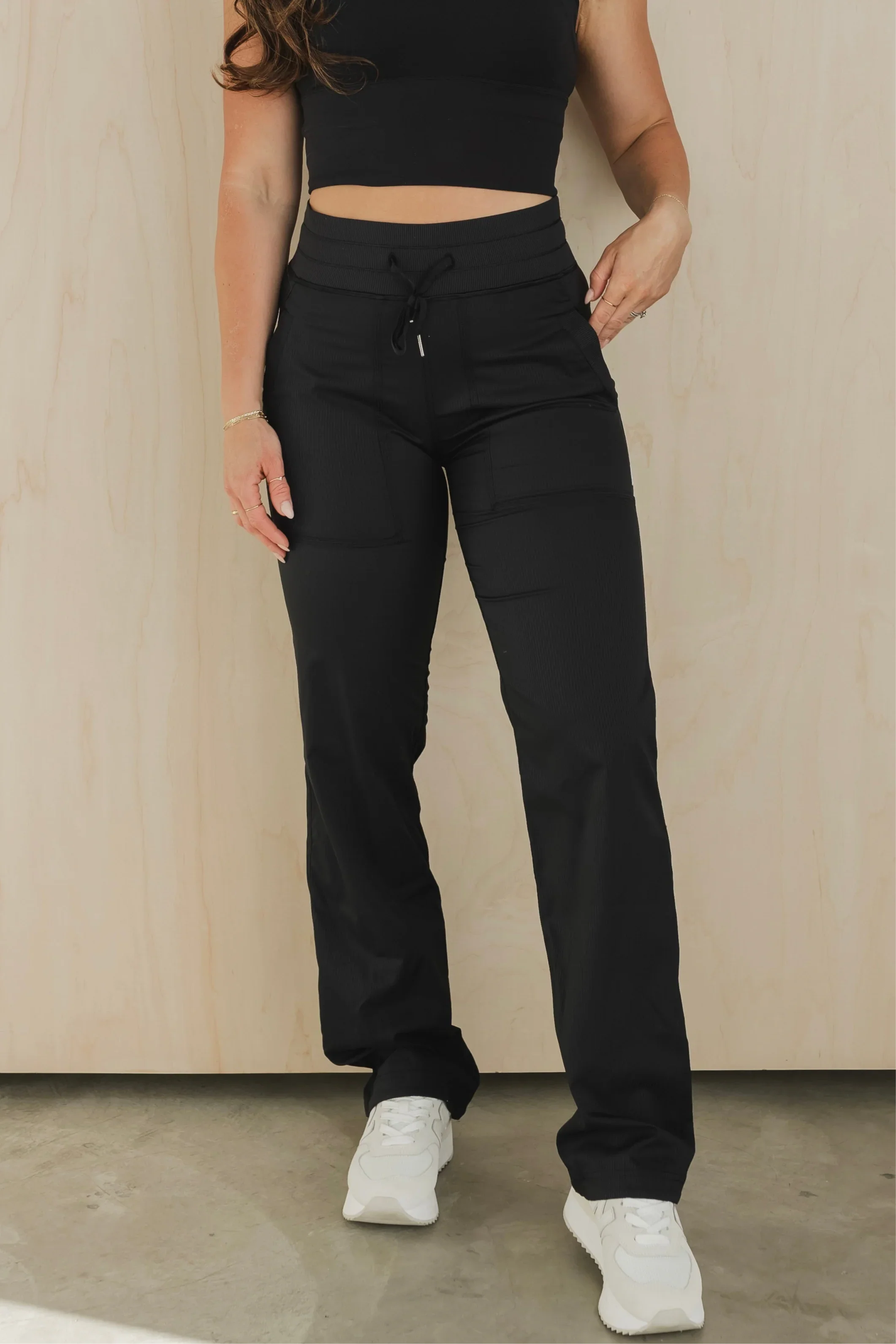 Woman wearing black drawstring lounge pants and white sneakers in front of a light wood wall