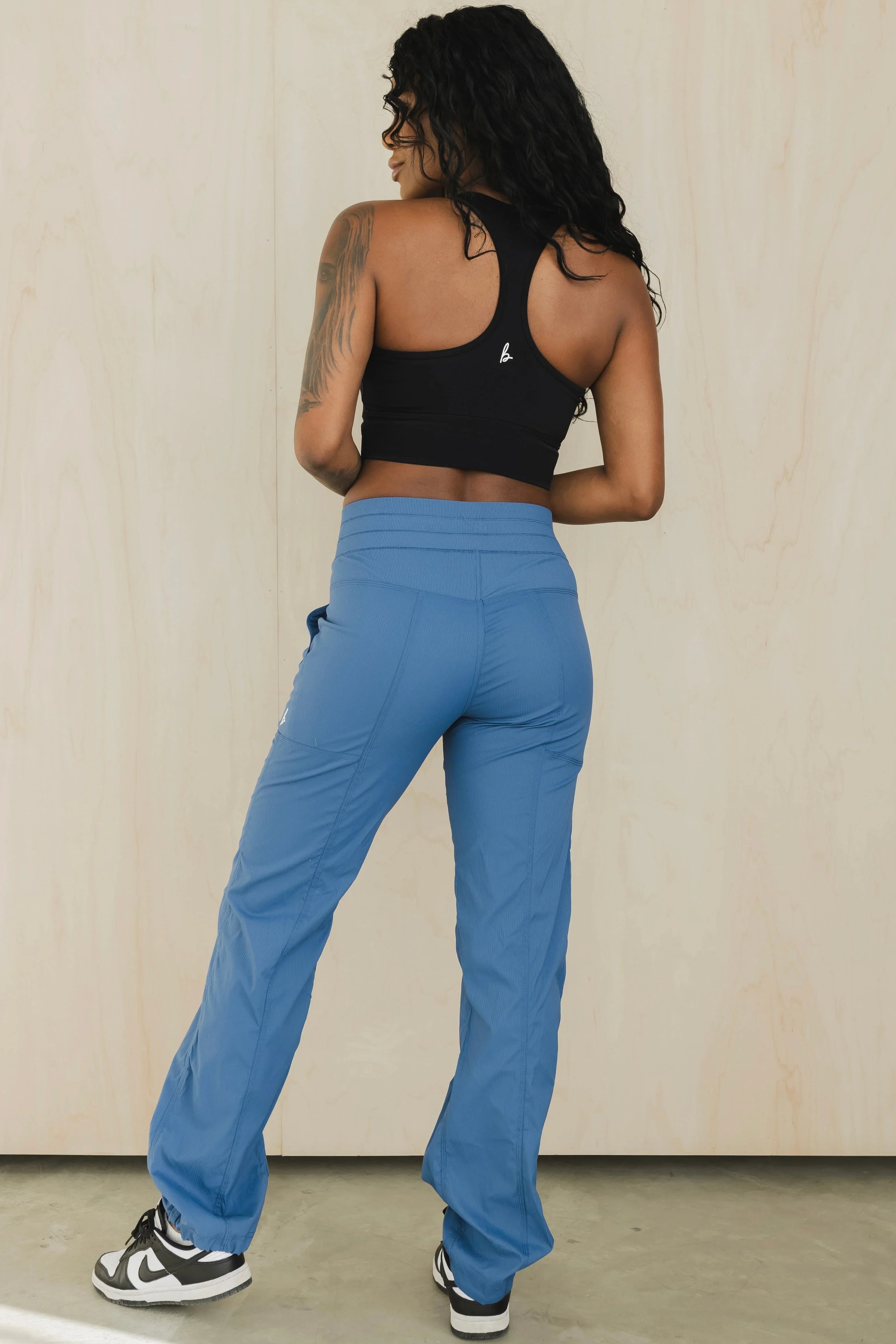 Woman in black racerback sports bra and blue jogger pants, standing indoors