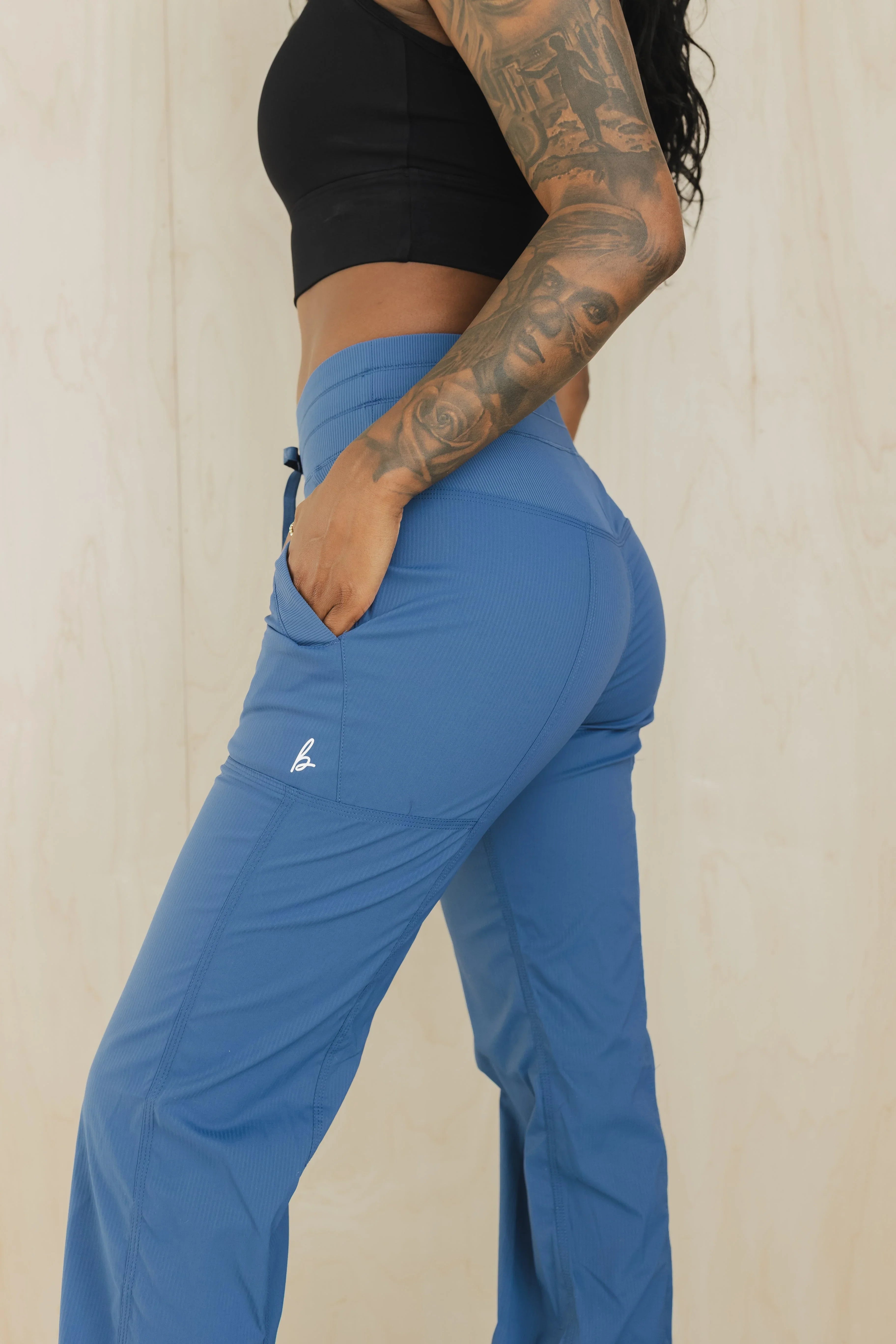 Woman in blue high-waisted athletic pants with pocket, black crop top, and arm tattoos
