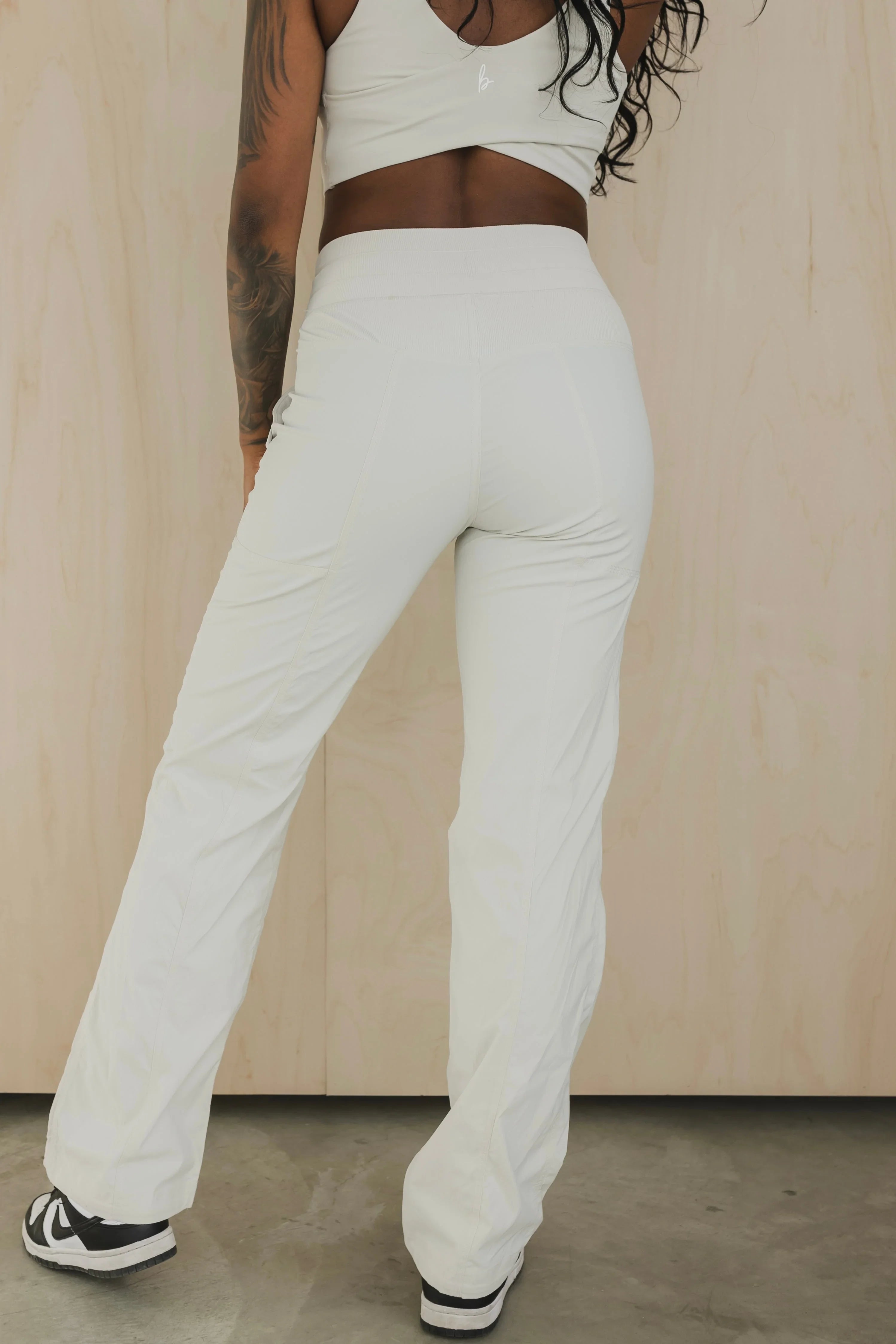 Woman in white athletic pants and crop top with tattoo, standing indoors on concrete floor