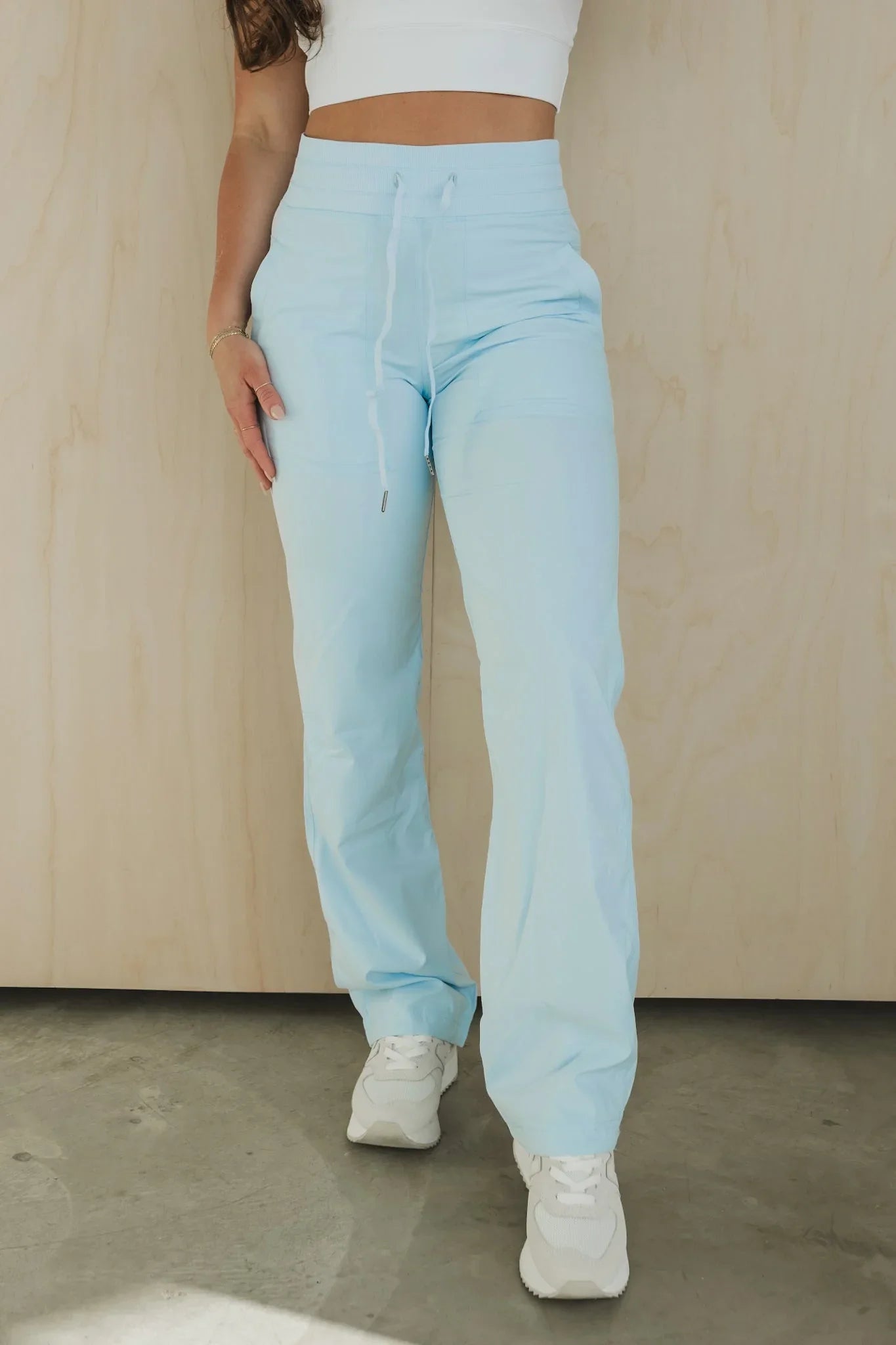 Woman wearing light blue jogger pants, white crop top, and sneakers against wood background