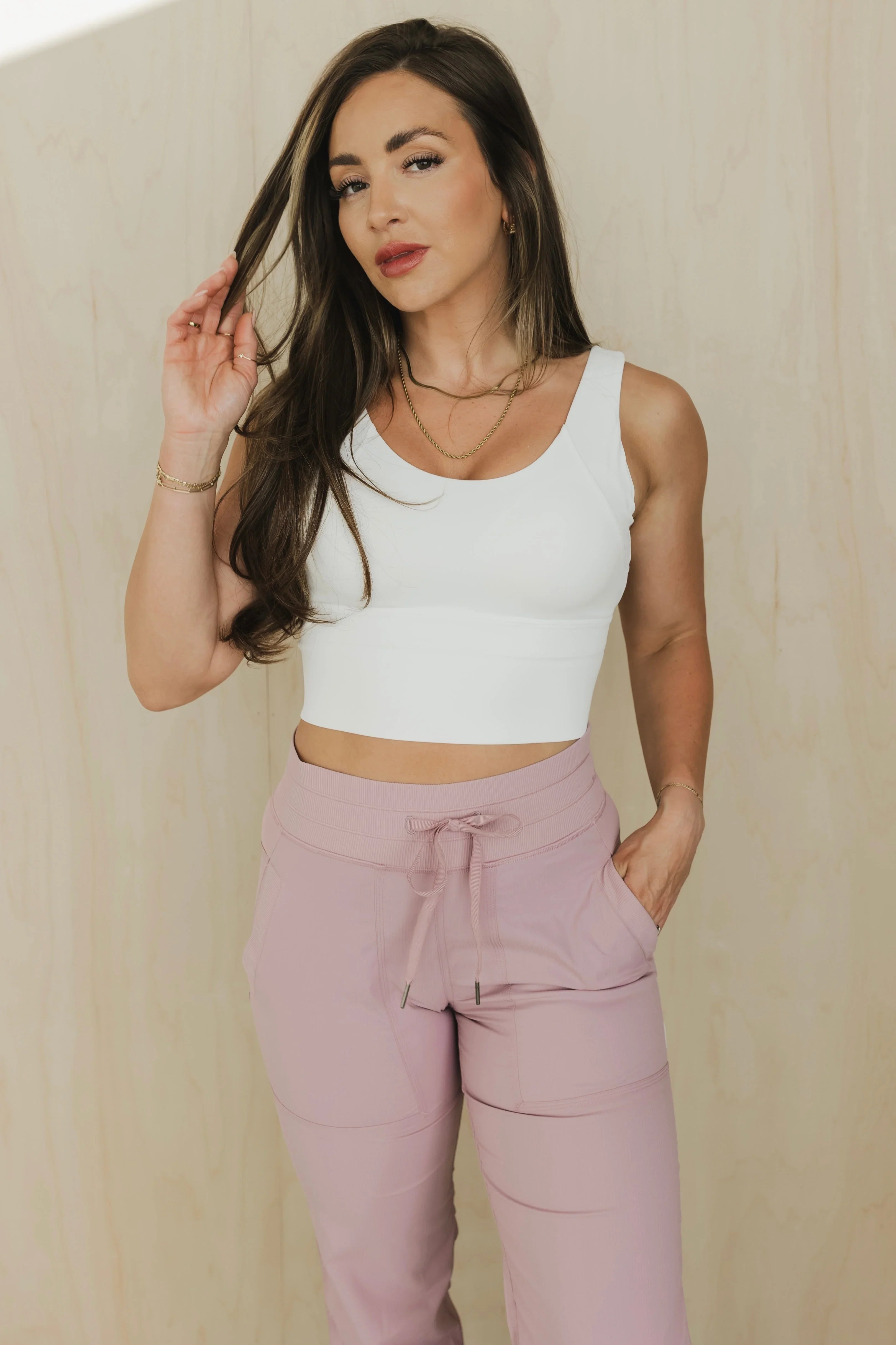 Woman in white crop top and pink drawstring pants posing against beige background