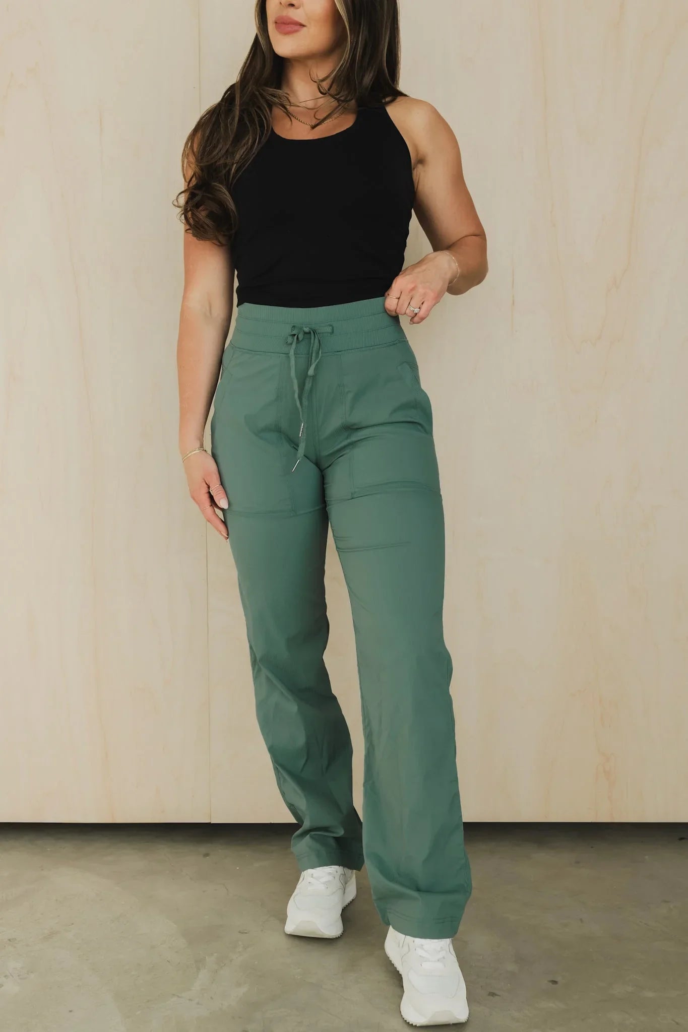 Woman wearing sage green drawstring joggers, black tank top, and white sneakers