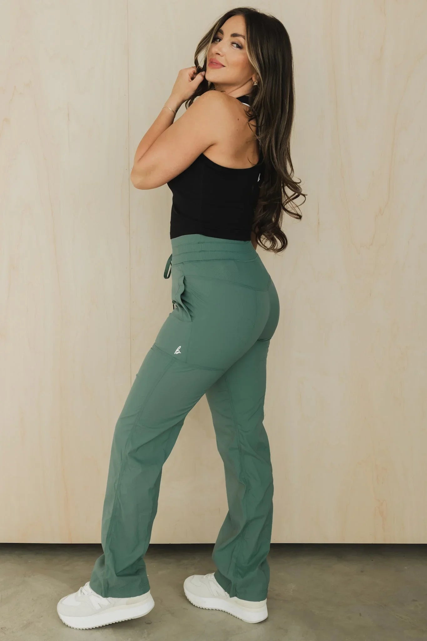 Woman modeling green high-waisted jogger pants, black tank top, and white sneakers indoors