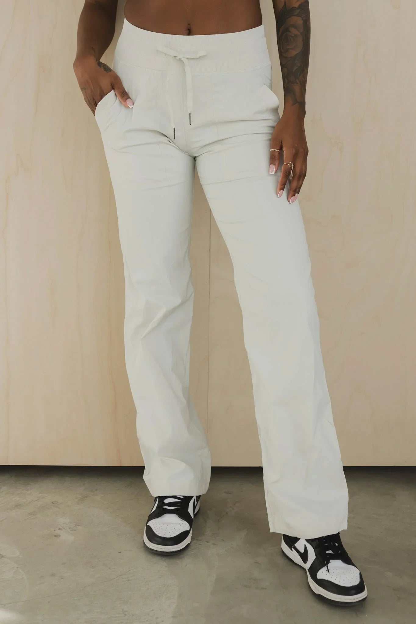 Woman wearing white drawstring pants and black sneakers standing indoors