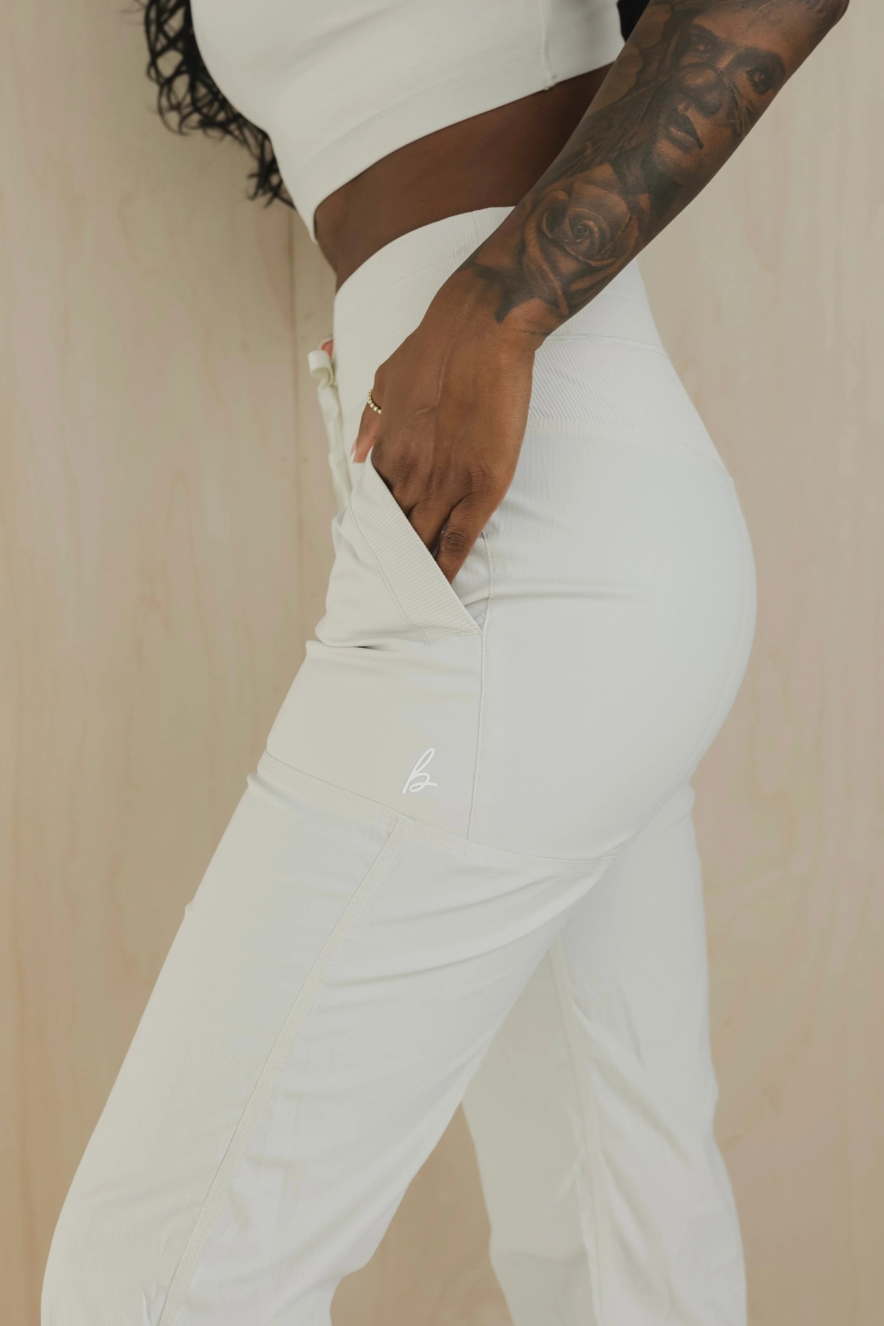 Woman wearing white high-waisted pants with front pocket and tattooed arm