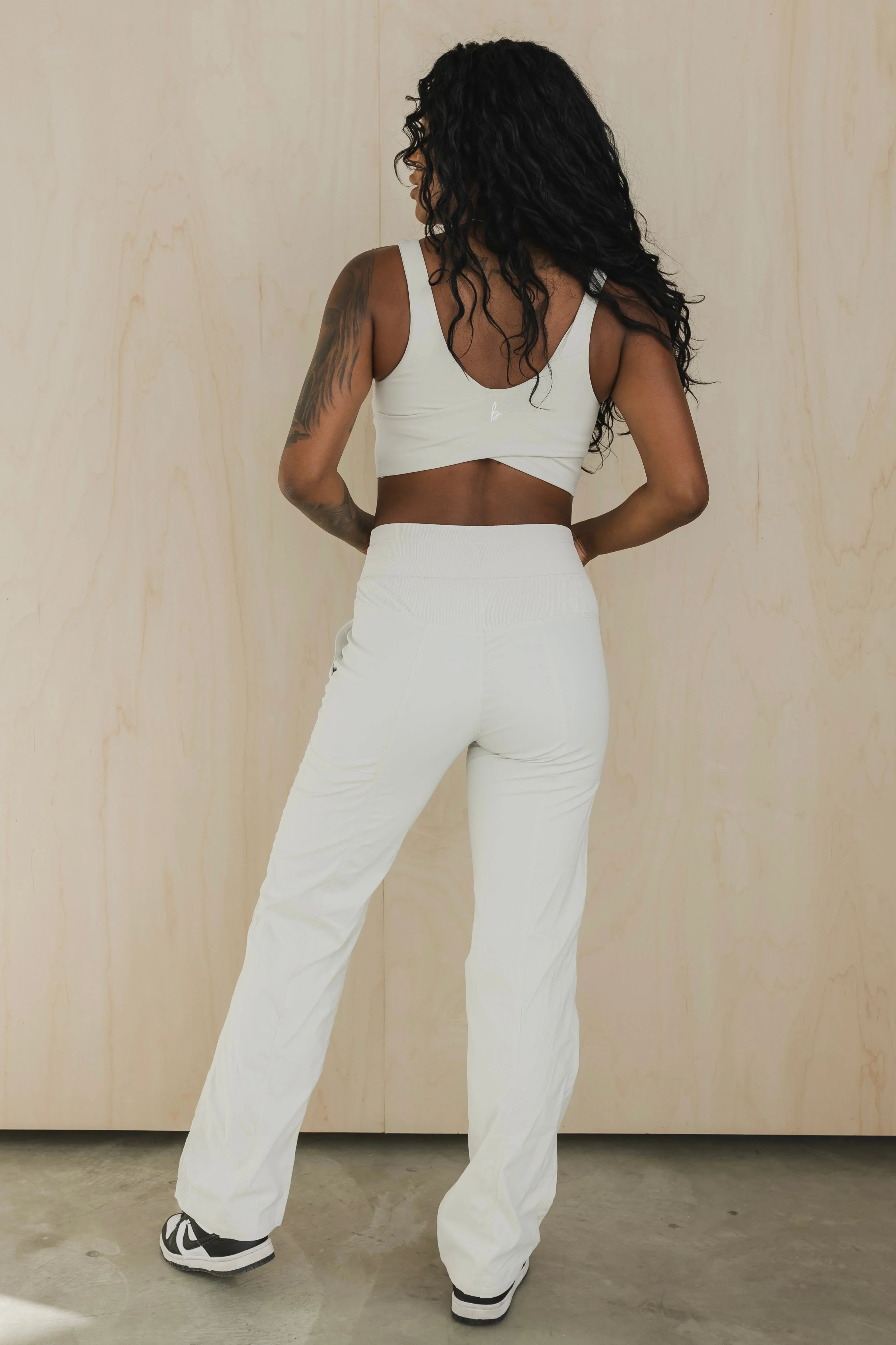 Woman in white activewear set with tattoo, standing on concrete floor, wood background