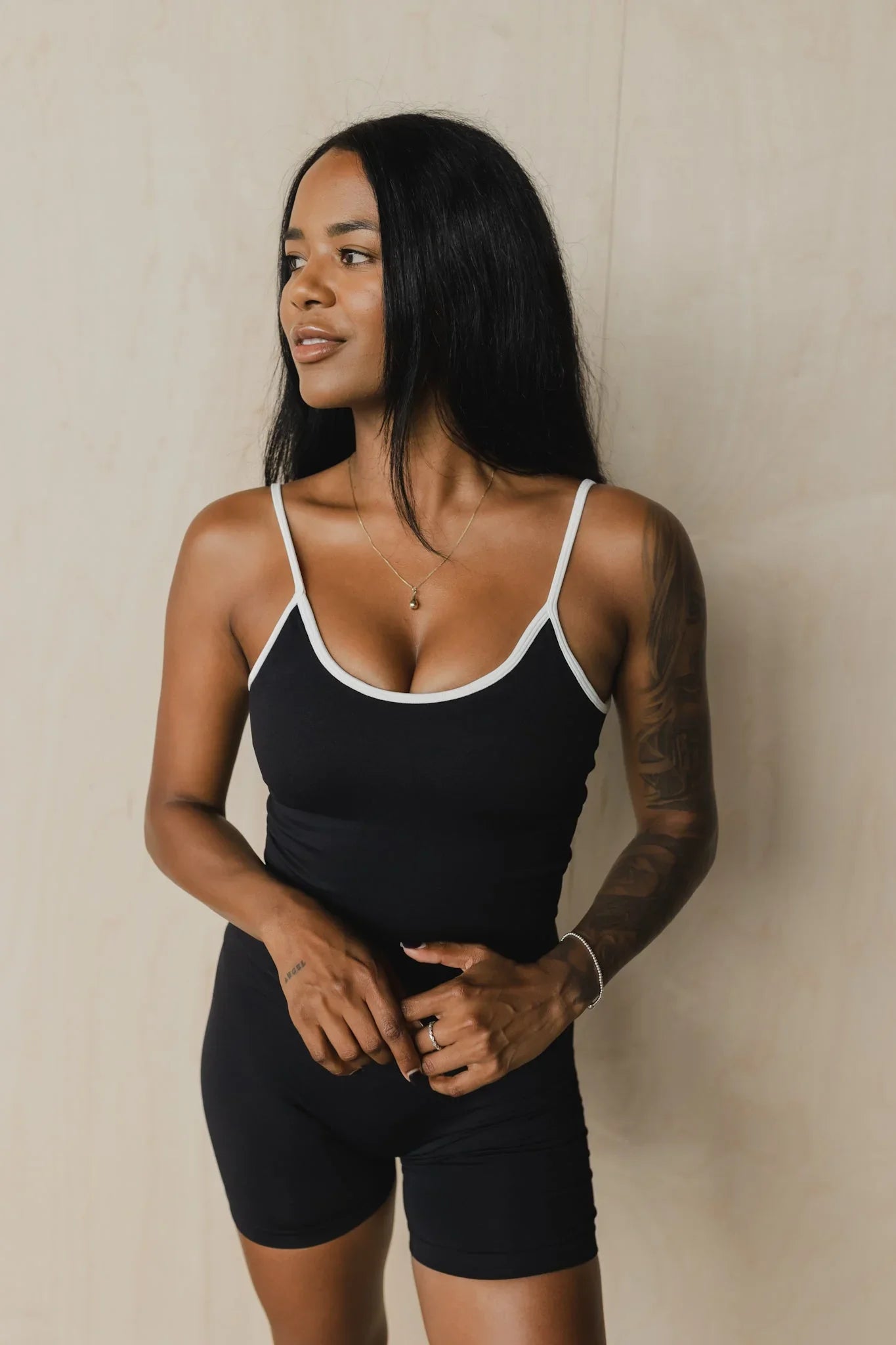 Woman in black athletic romper with white trim, standing against beige background