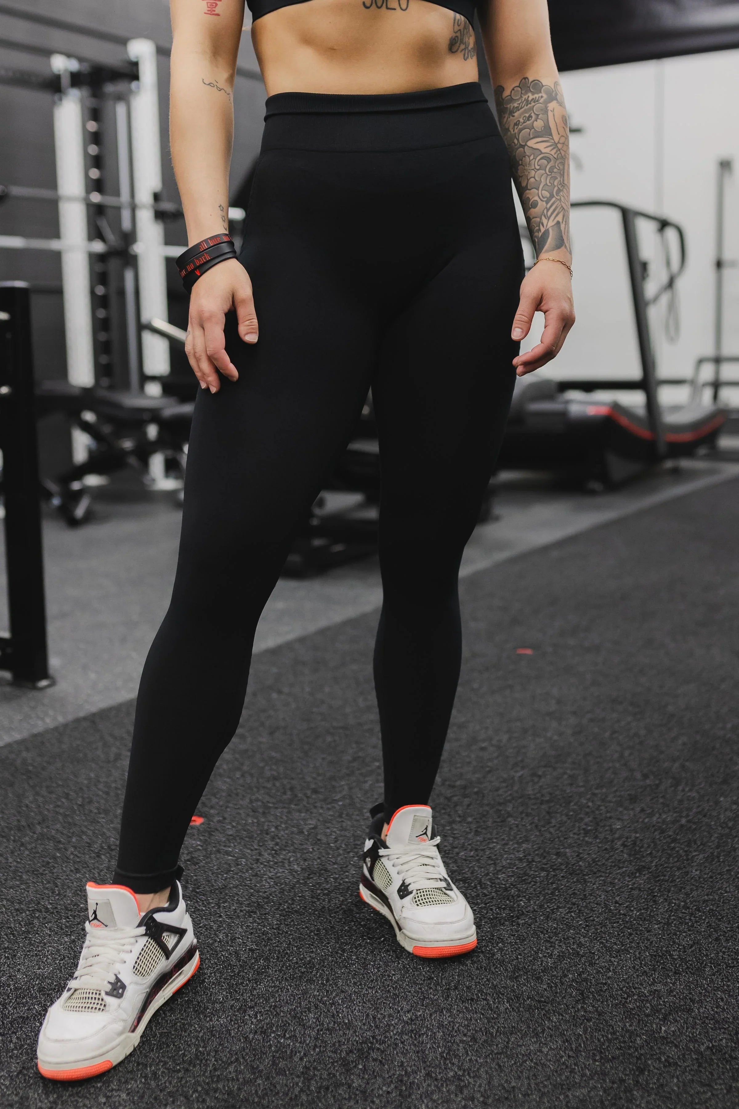 Woman in black high-waisted leggings and white sneakers standing in gym