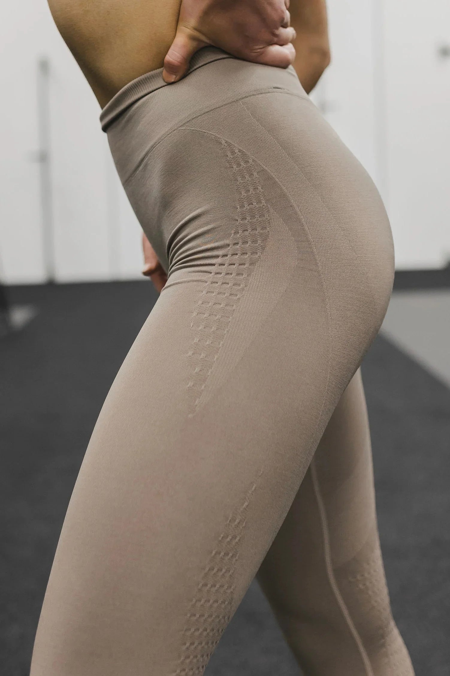 Beige seamless high-waisted leggings in gym setting, close-up on textured fabric