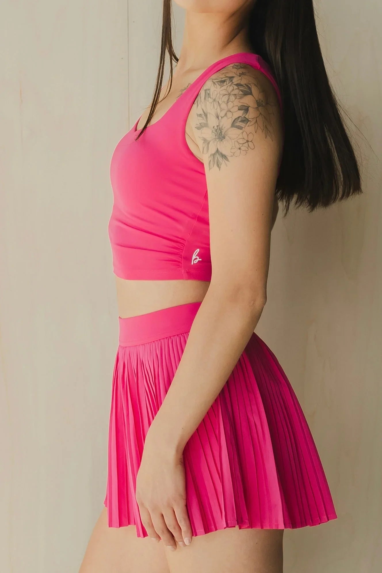 Woman in pink sports crop top and pleated skirt with floral arm tattoo