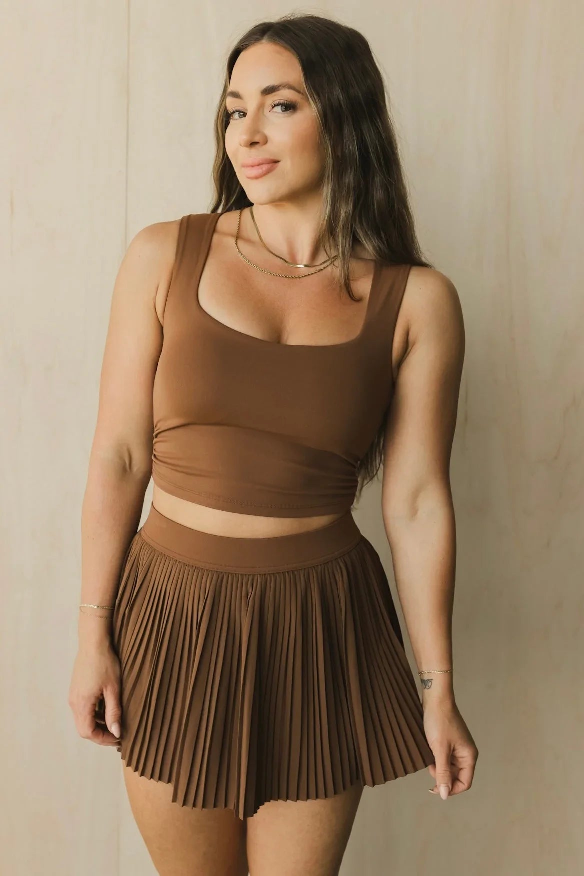 Woman wearing brown crop top and pleated mini skirt, neutral background