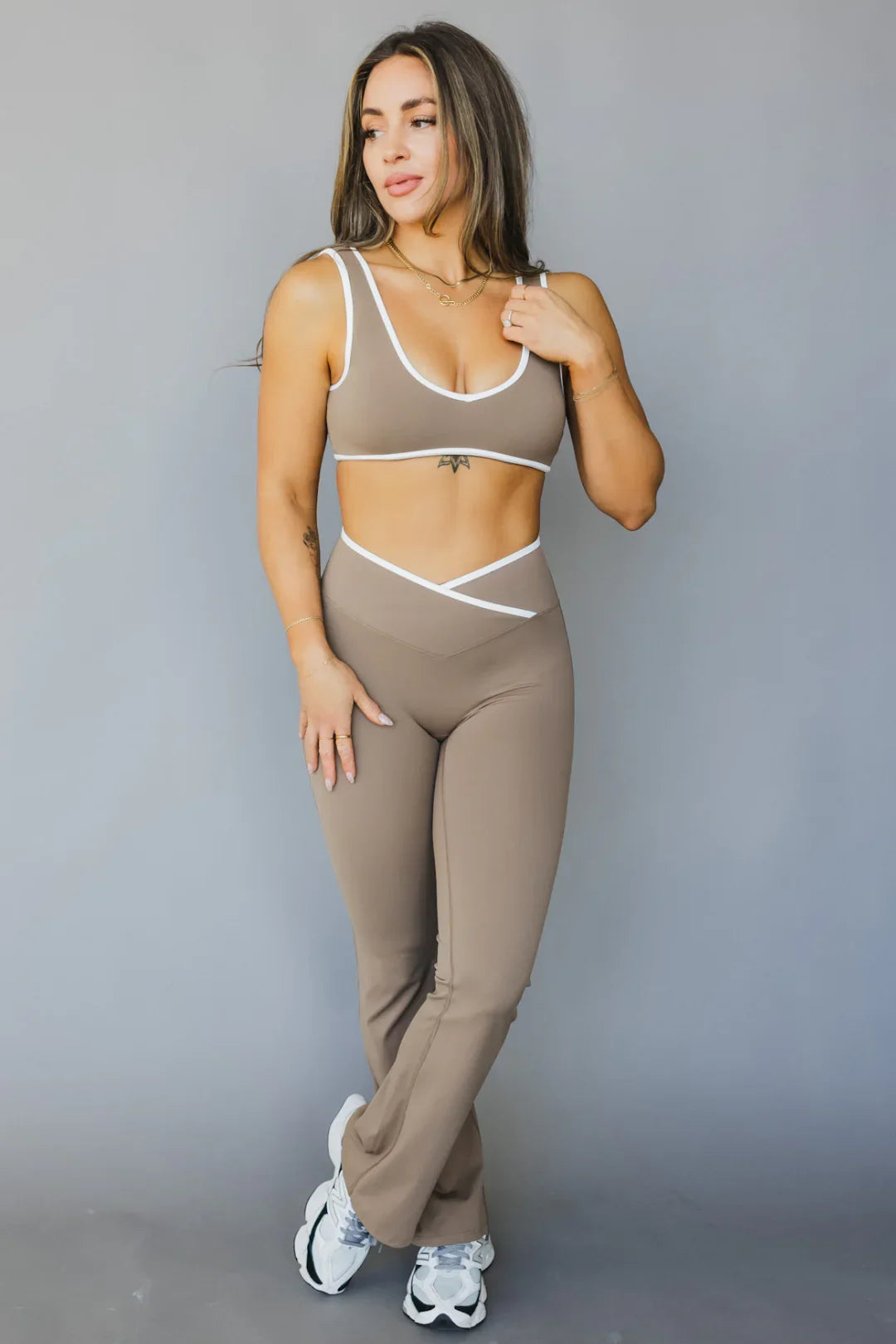 Woman modeling taupe athletic matching set with white trim and sneakers against gray background