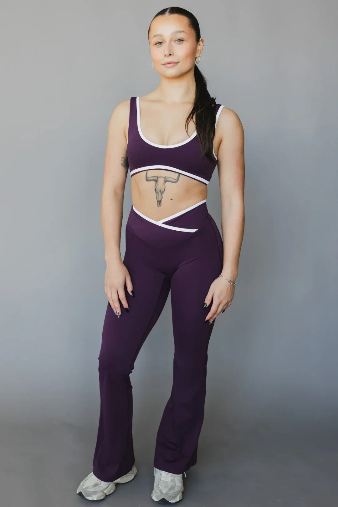 Woman in purple matching yoga set with white trim, posing against gray background