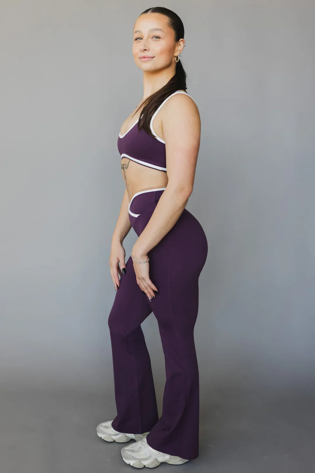 Woman in purple yoga set with white trim posing in studio, athletic wear fashion