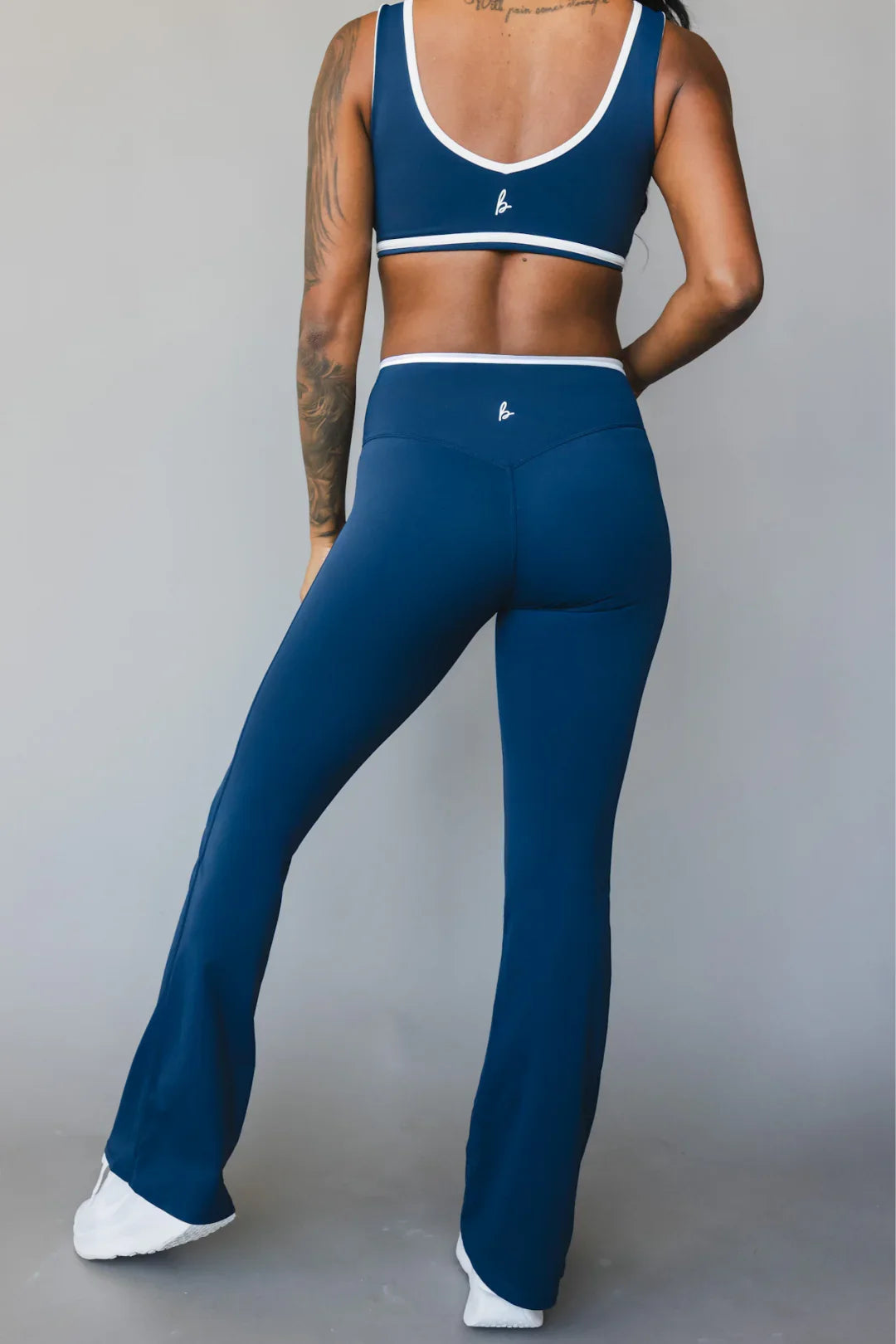 Woman in blue athletic set with white trim, flared leggings, sports bra, studio background