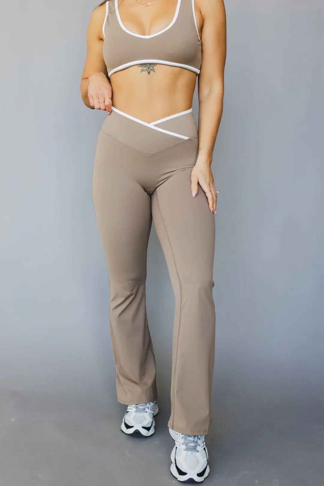 Woman modeling taupe workout set with white trim and flared leggings against a gray background